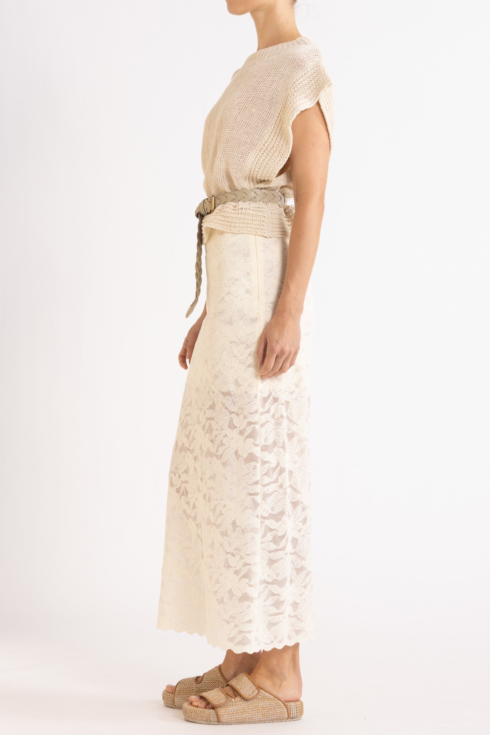 Woman wearing an Oat linen vest with a braided cream belt and a white floral lace maxi skirt