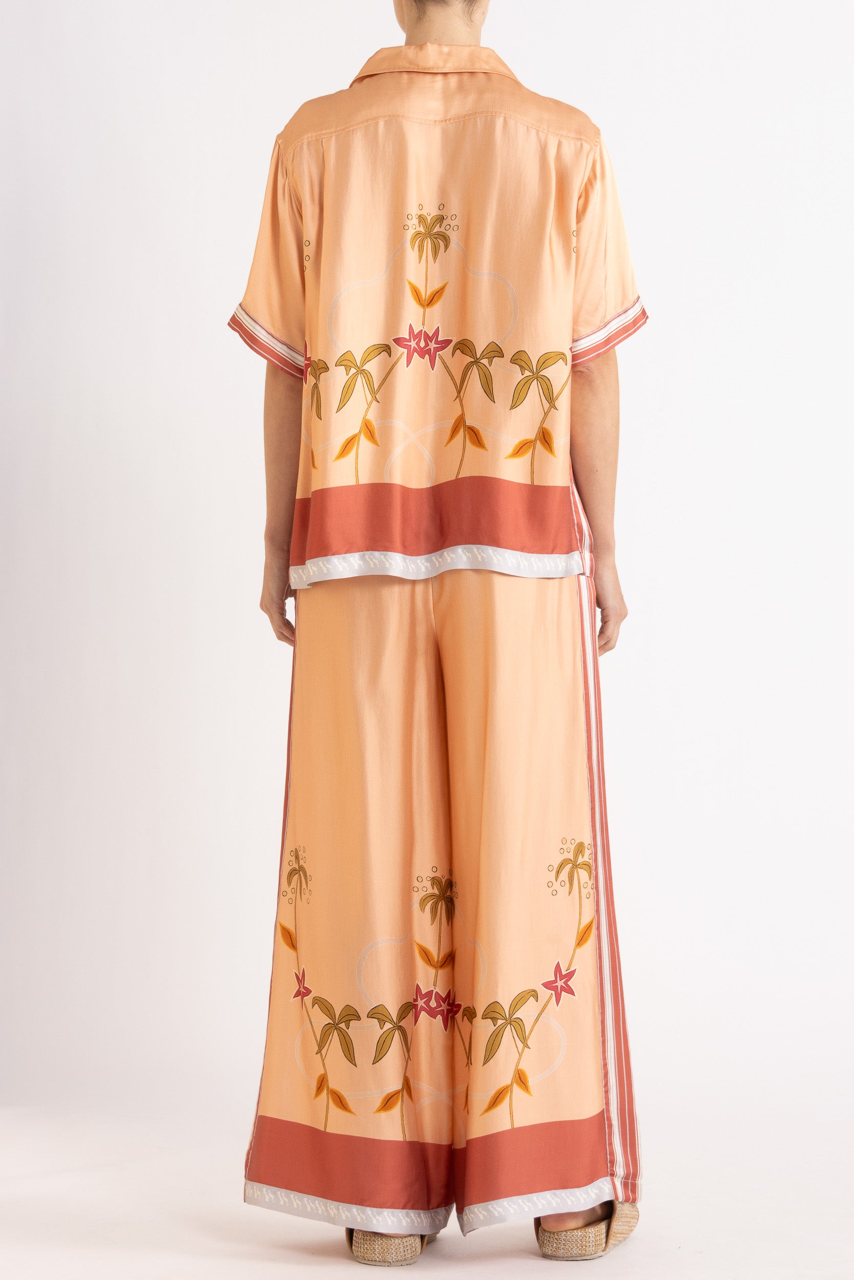 Woman wearing a matching peach short sleeve shirt and pants featuring floral patterns on a white background