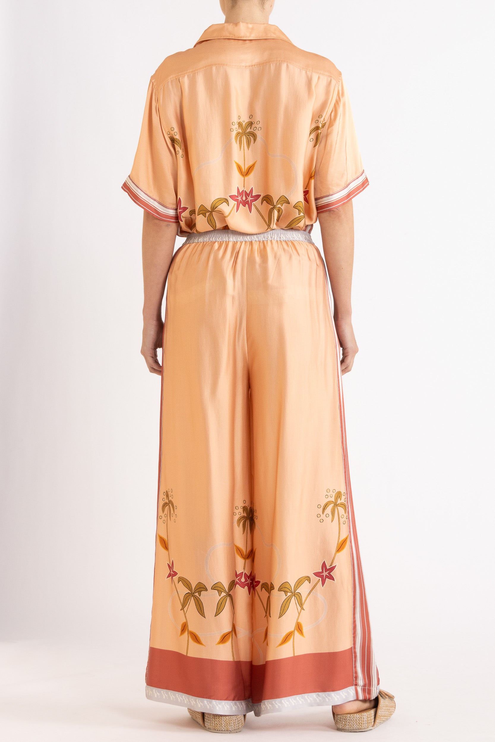 Woman wearing a matching peach short sleeve shirt and pants featuring floral patterns on a white background