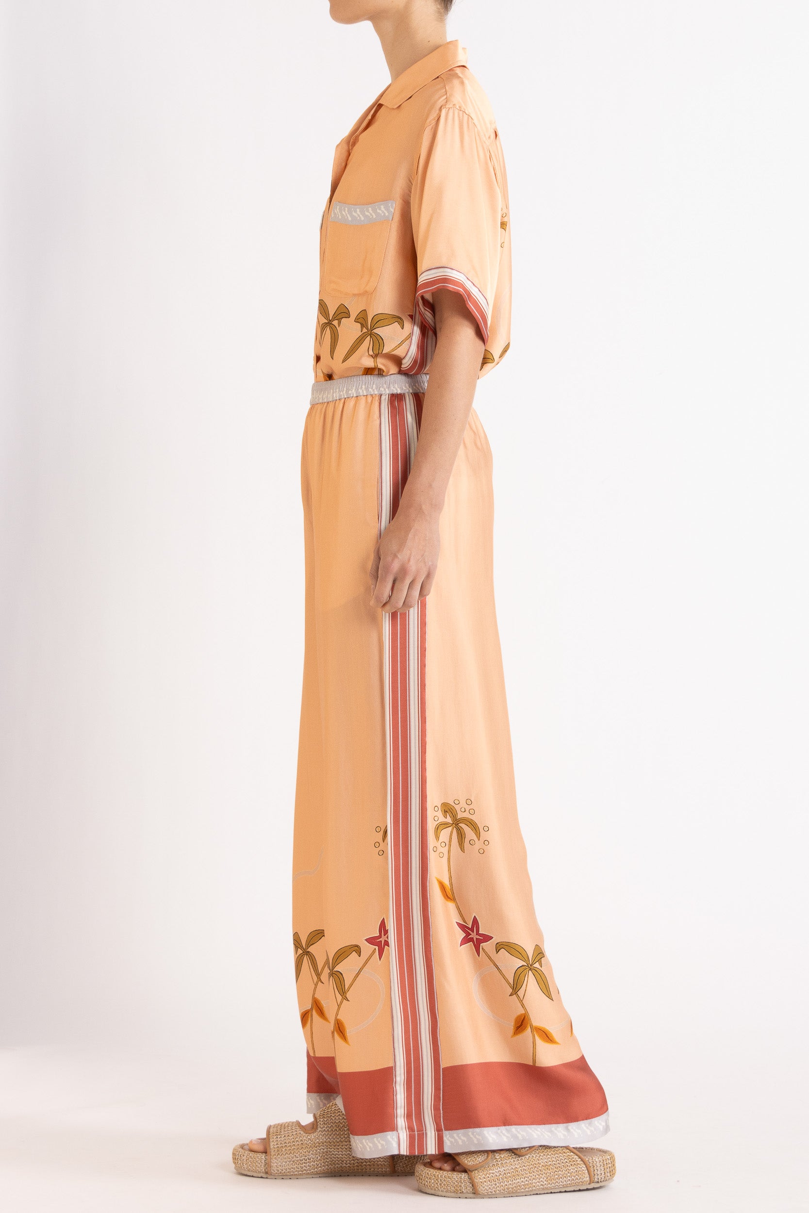 Woman wearing a matching peach short sleeve shirt and pants featuring floral patterns on a white background