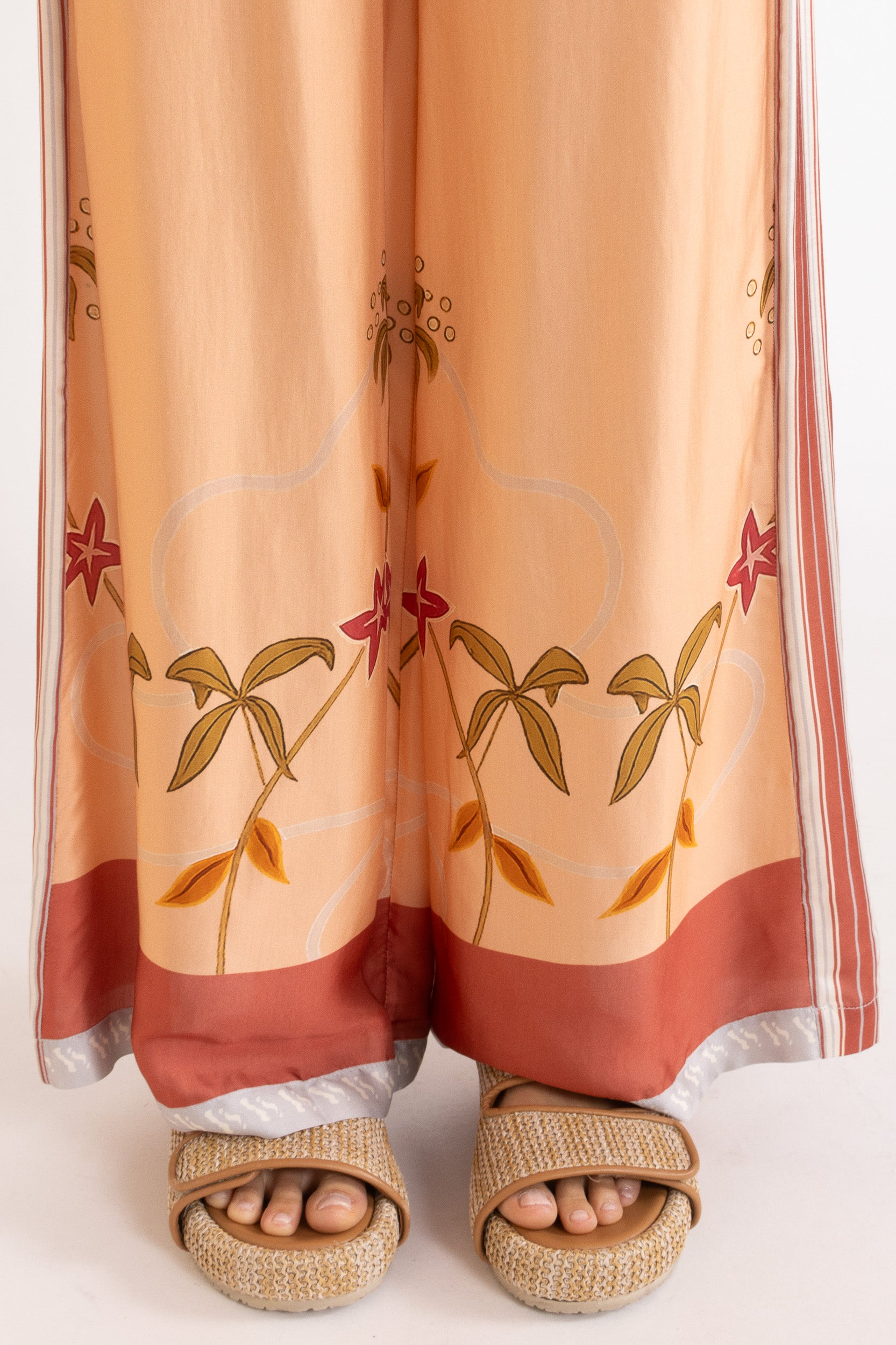 Woman wearing peach pants featuring floral patterns on a white background