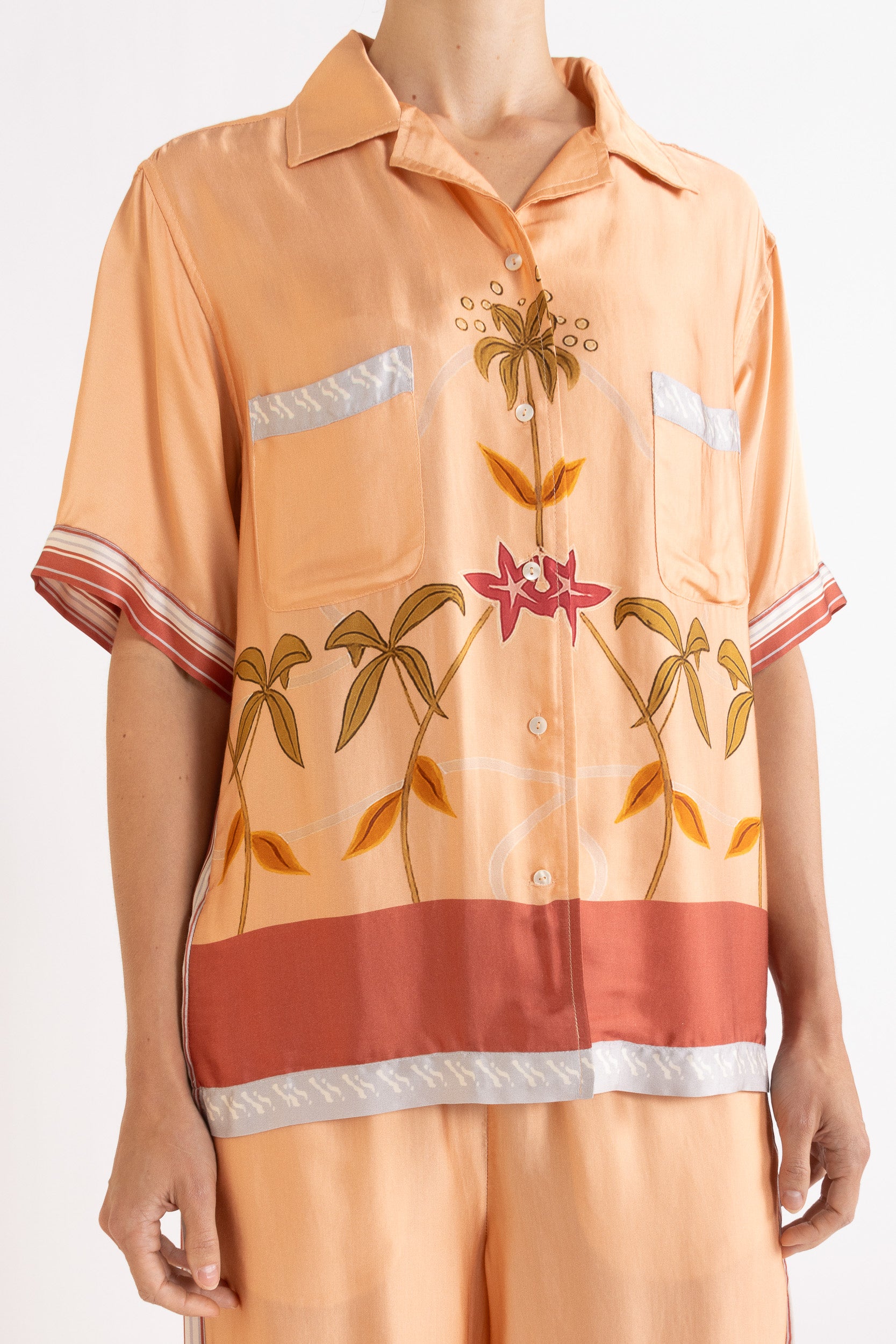 Woman wearing a peach shirt with floral and leaf patterns on a white background