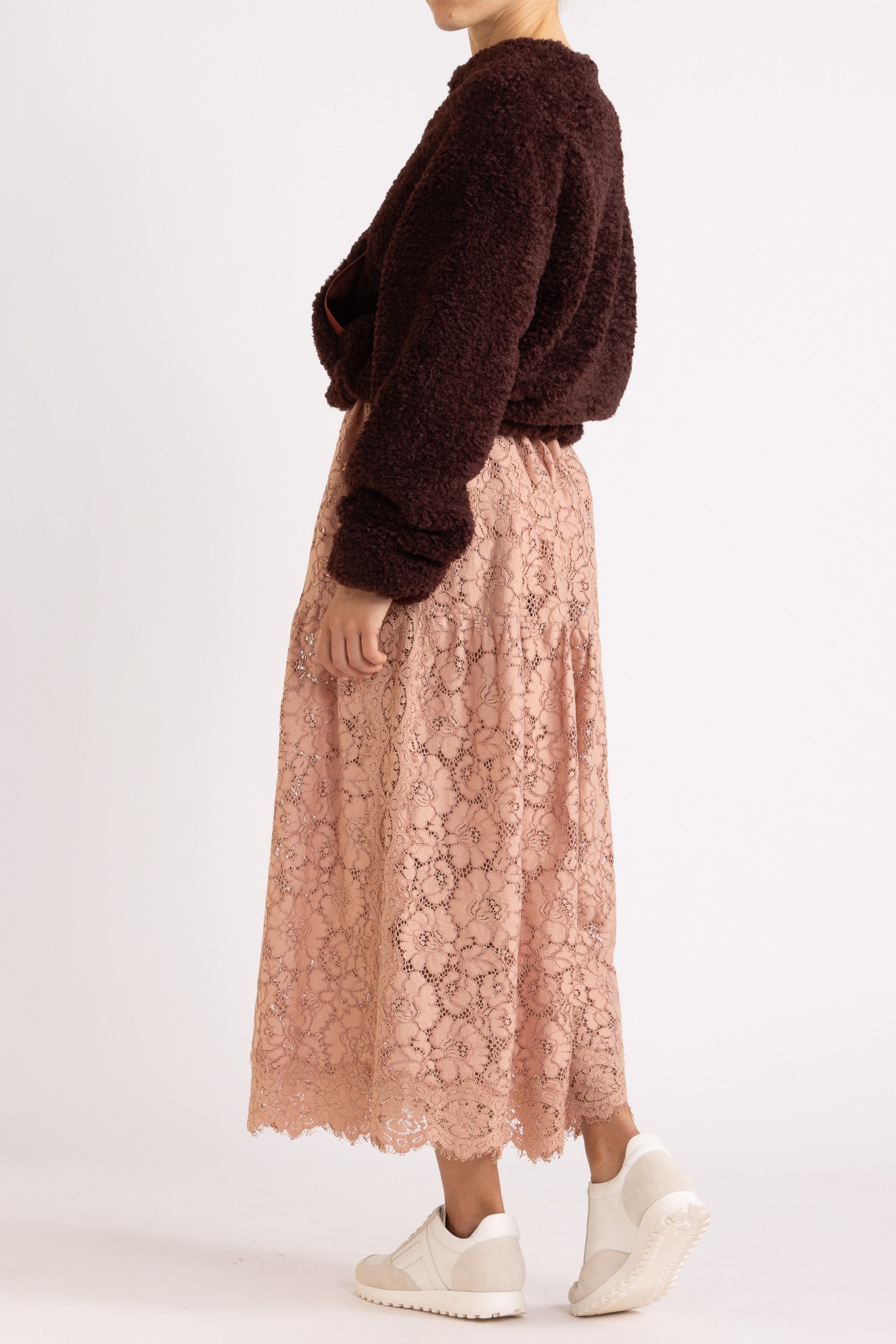 Woman wearing a port coloured faux fur jacket with a rouge floral lace maxi dress on a white background