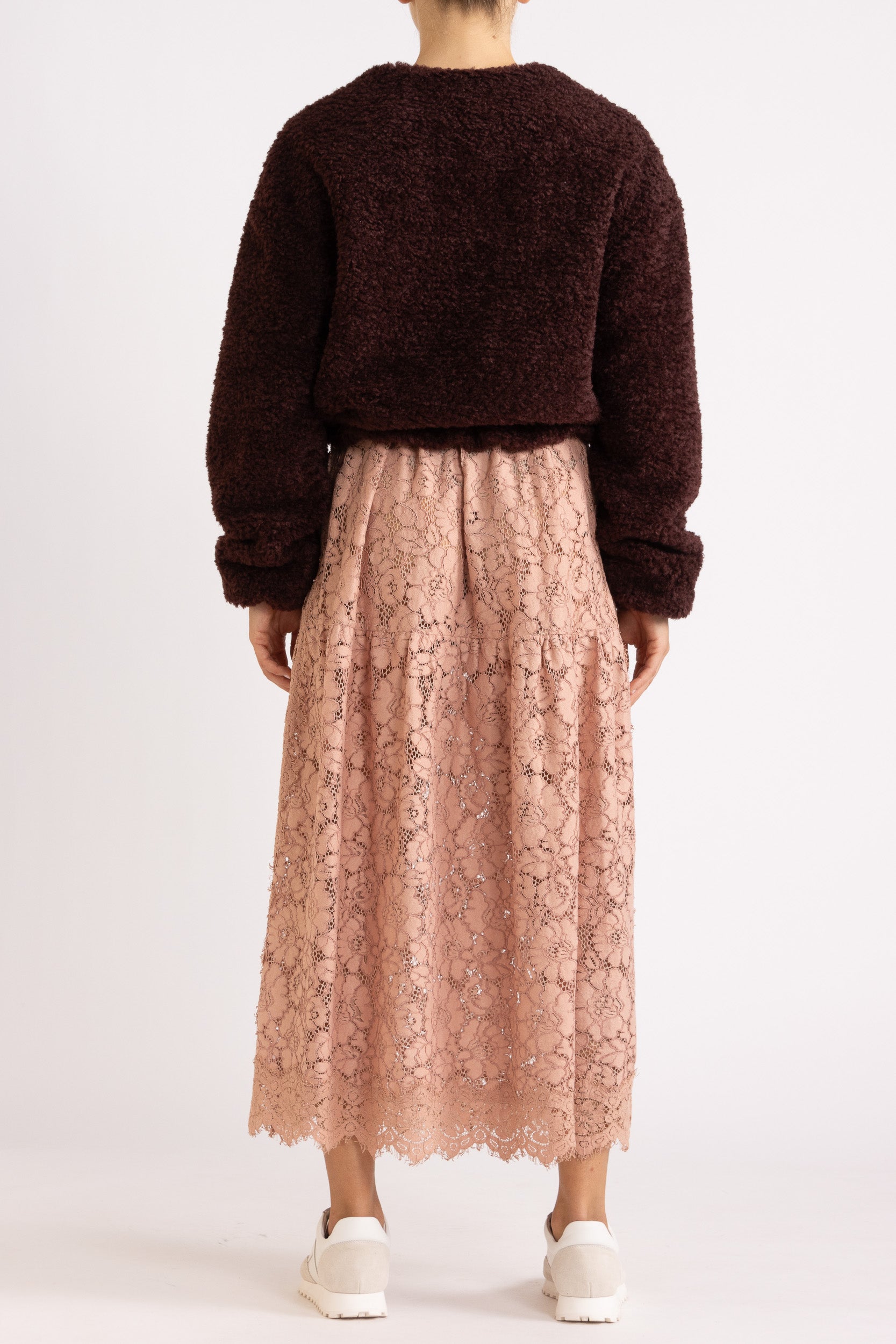 Woman wearing a port coloured faux fur jacket with a rouge floral lace maxi dress on a white background