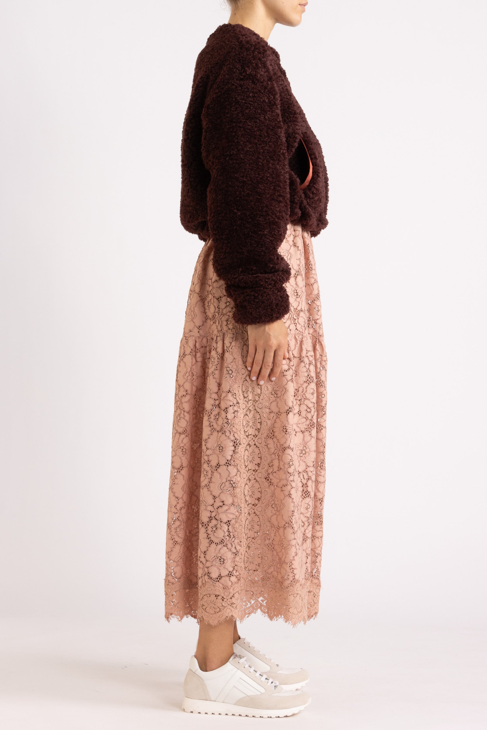 Woman wearing a port coloured faux fur jacket with a rouge floral lace maxi dress on a white background