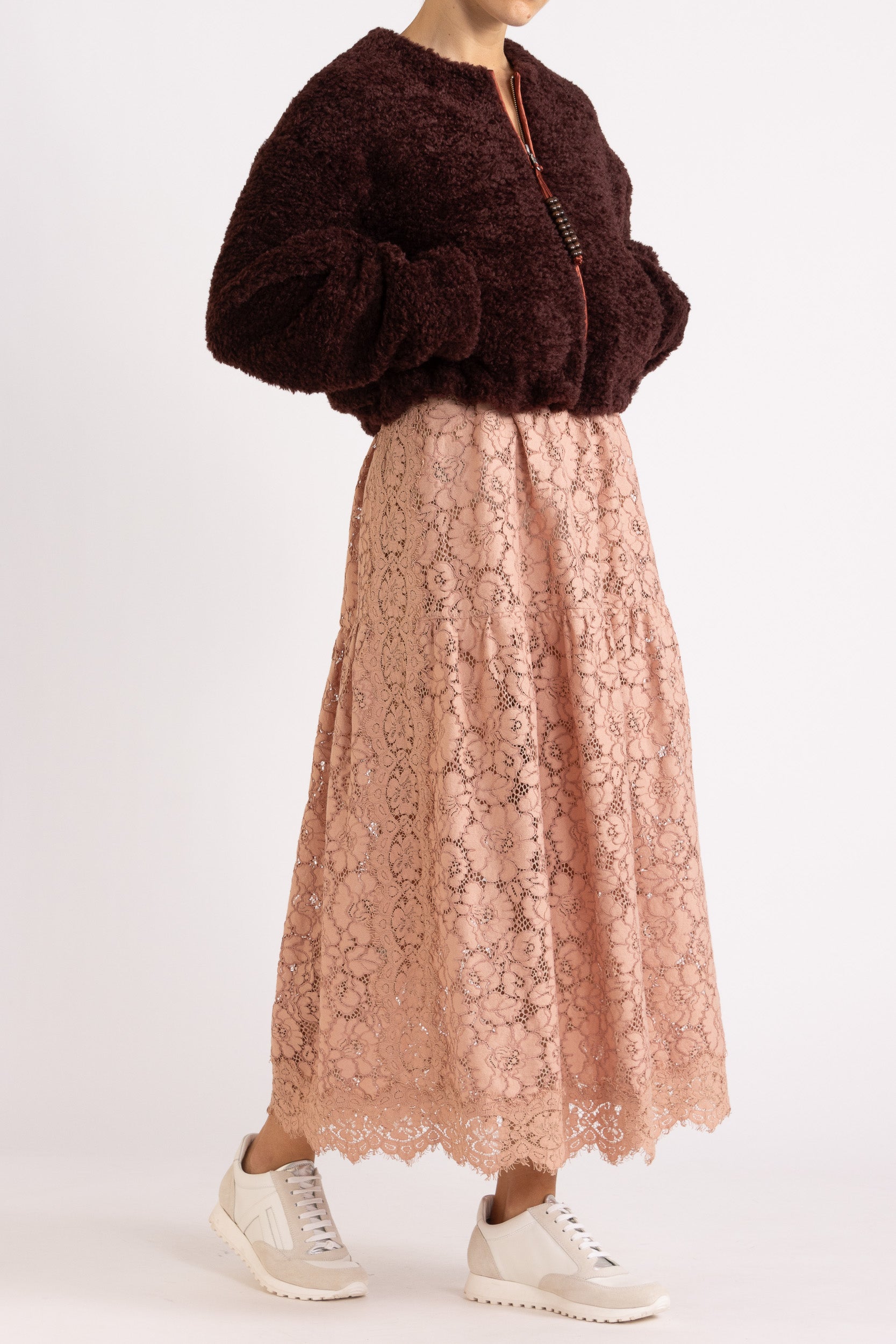 Woman wearing a port coloured faux fur jacket with a rouge floral lace maxi dress on a white background