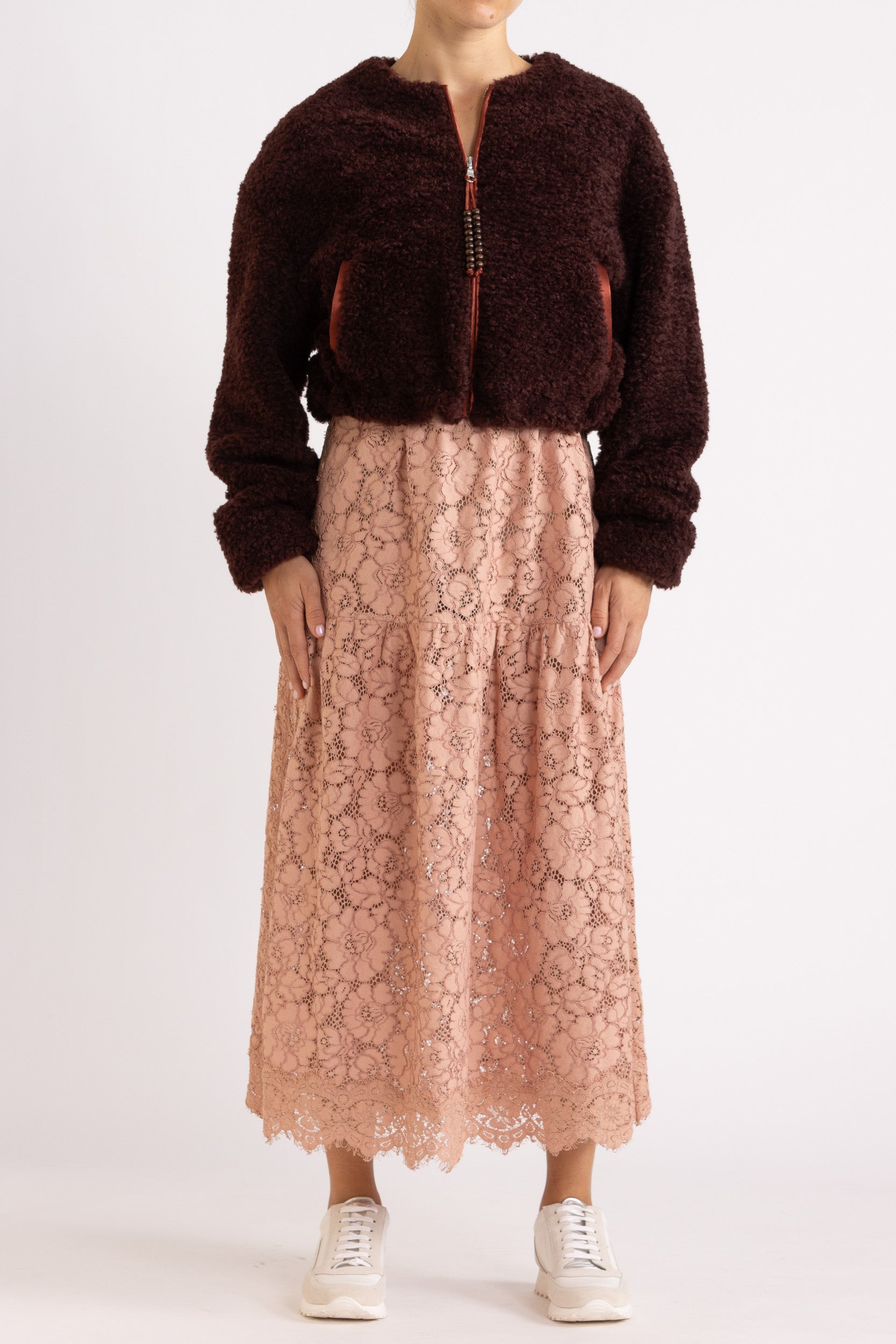 Woman wearing a port coloured faux fur jacket with a rouge floral lace maxi dress on a white background