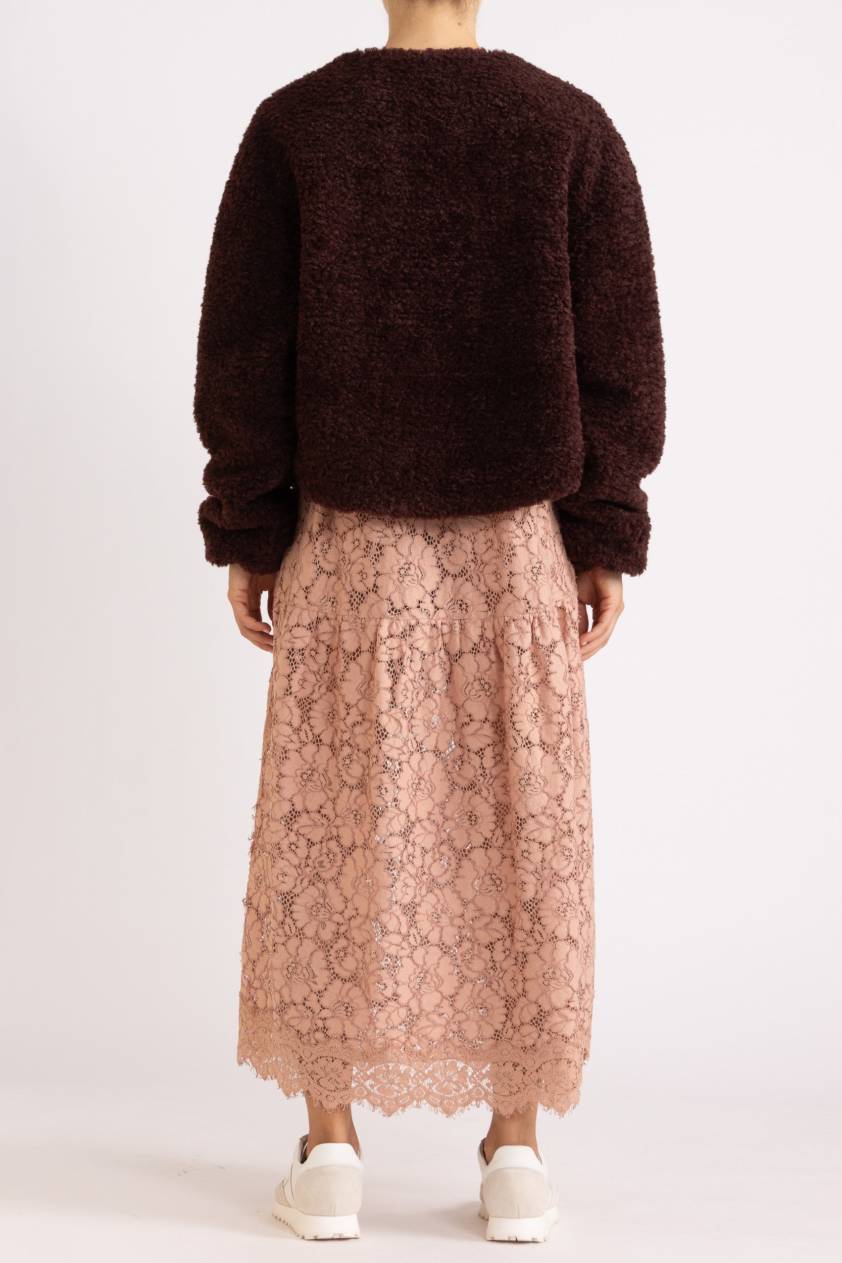 Woman wearing a port coloured faux fur jacket with a rouge floral lace maxi dress on a white background