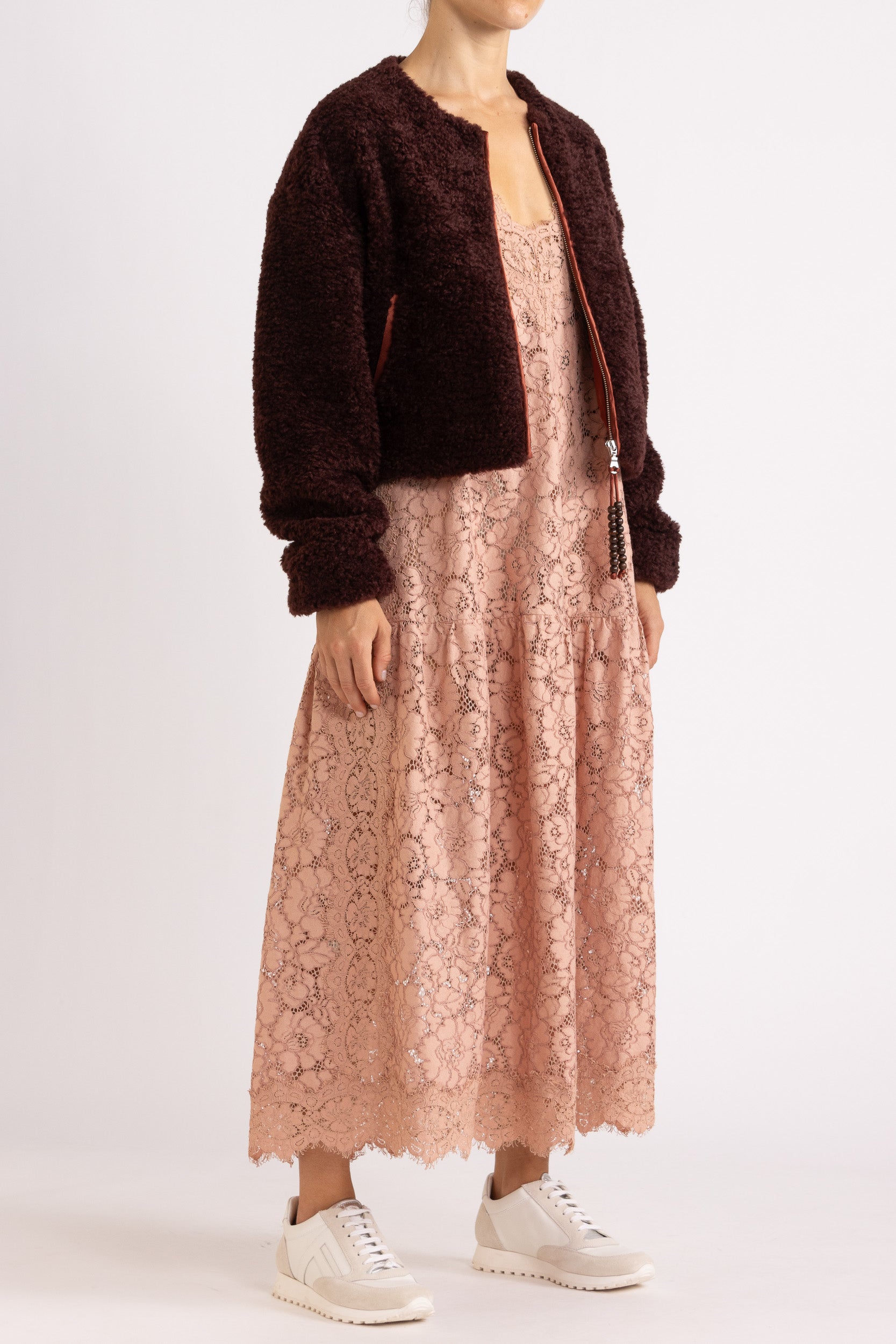 Woman wearing a port coloured faux fur jacket with a rouge floral lace maxi dress on a white background