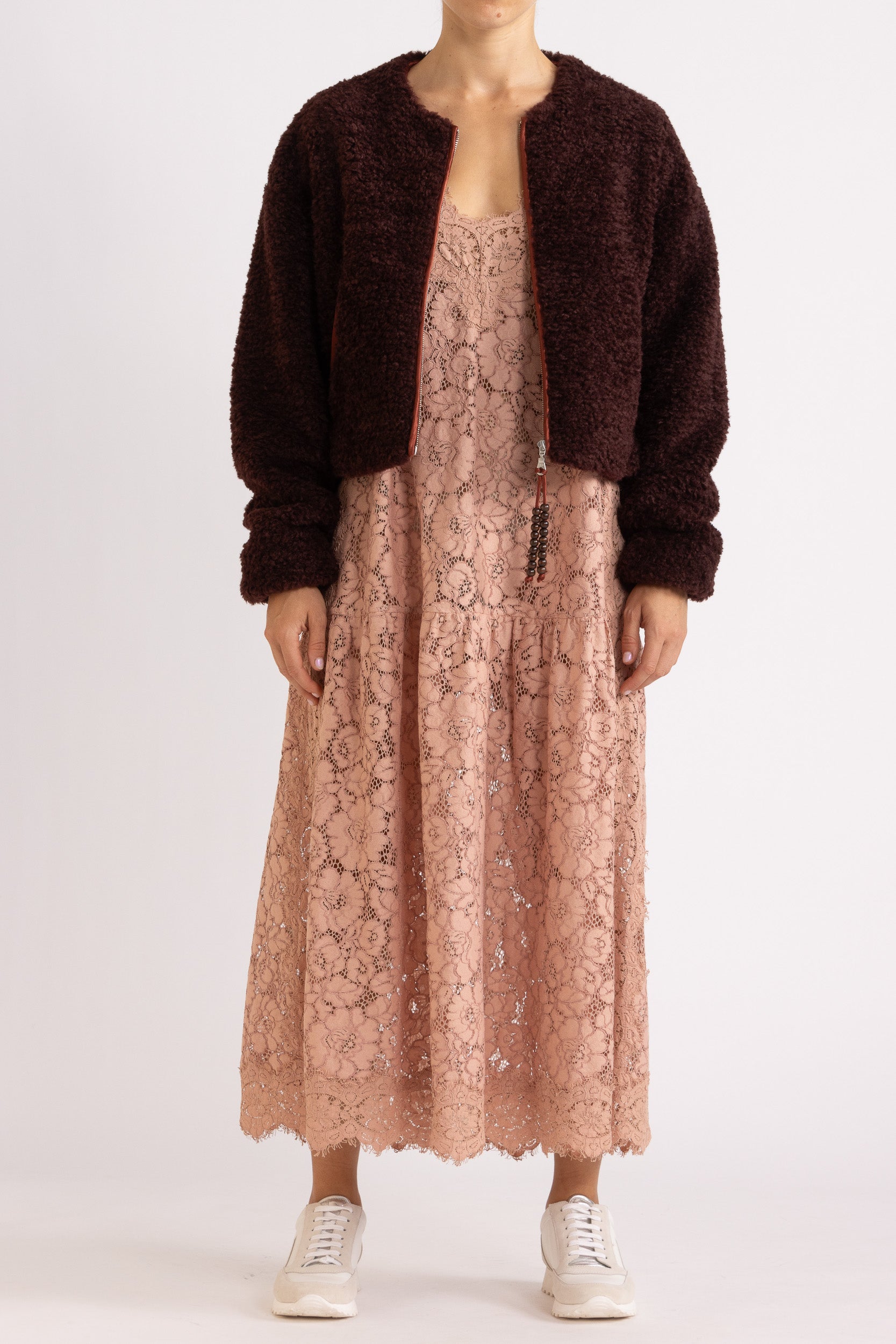 Woman wearing a port coloured faux fur jacket with a rouge floral lace maxi dress on a white background