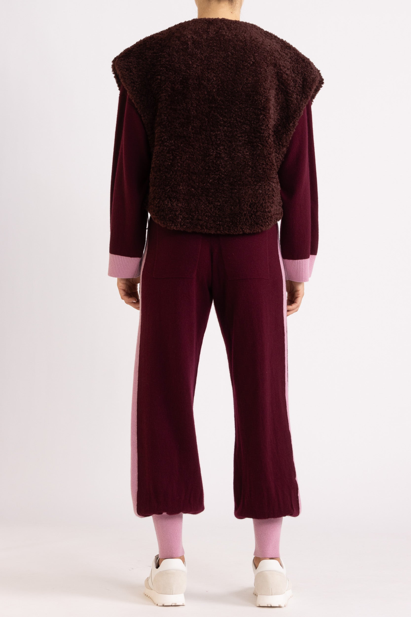 Woman wearing a faux fur vest in a port colour, layered over a aubergine coloured cashmere track pant and sweater set