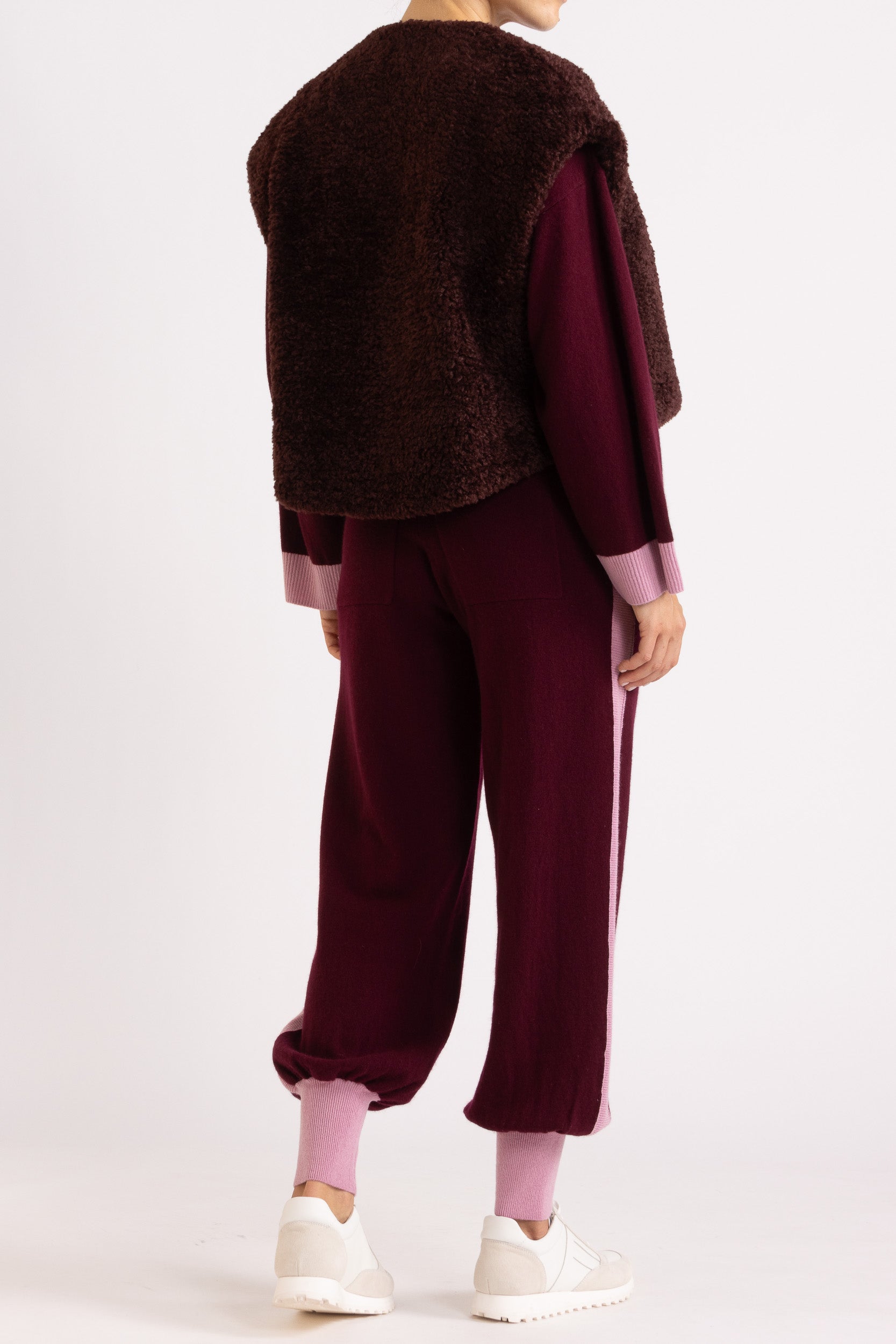 Woman wearing a faux fur vest in a port colour, layered over a aubergine coloured cashmere track pant and sweater set
