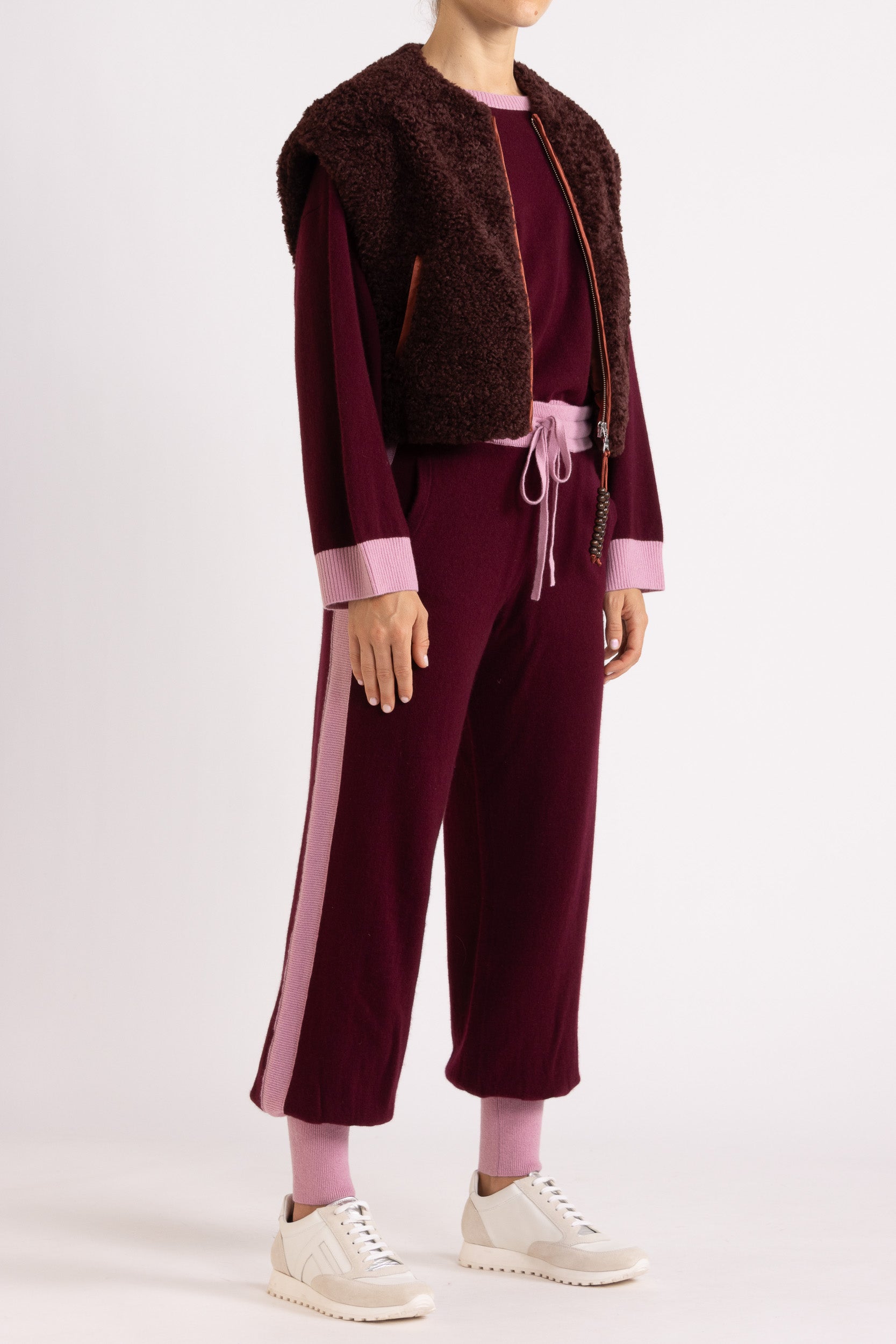 Woman wearing a faux fur vest in a port colour, layered over a aubergine coloured cashmere track pant and sweater set
