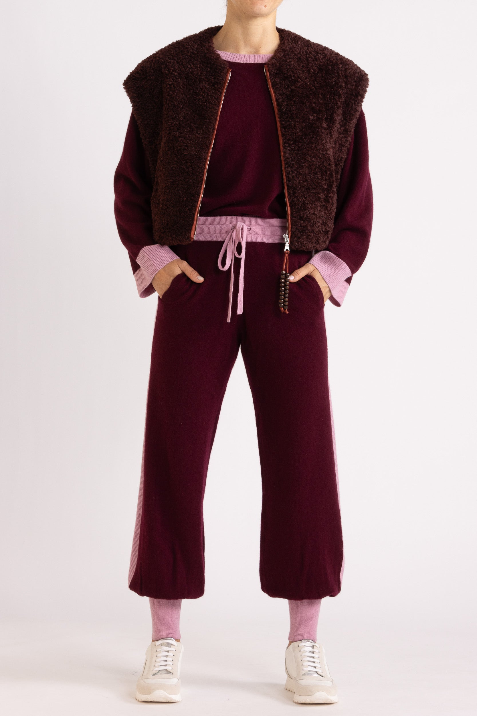 Woman wearing a faux fur vest in a port colour, layered over a aubergine coloured cashmere track pant and sweater set