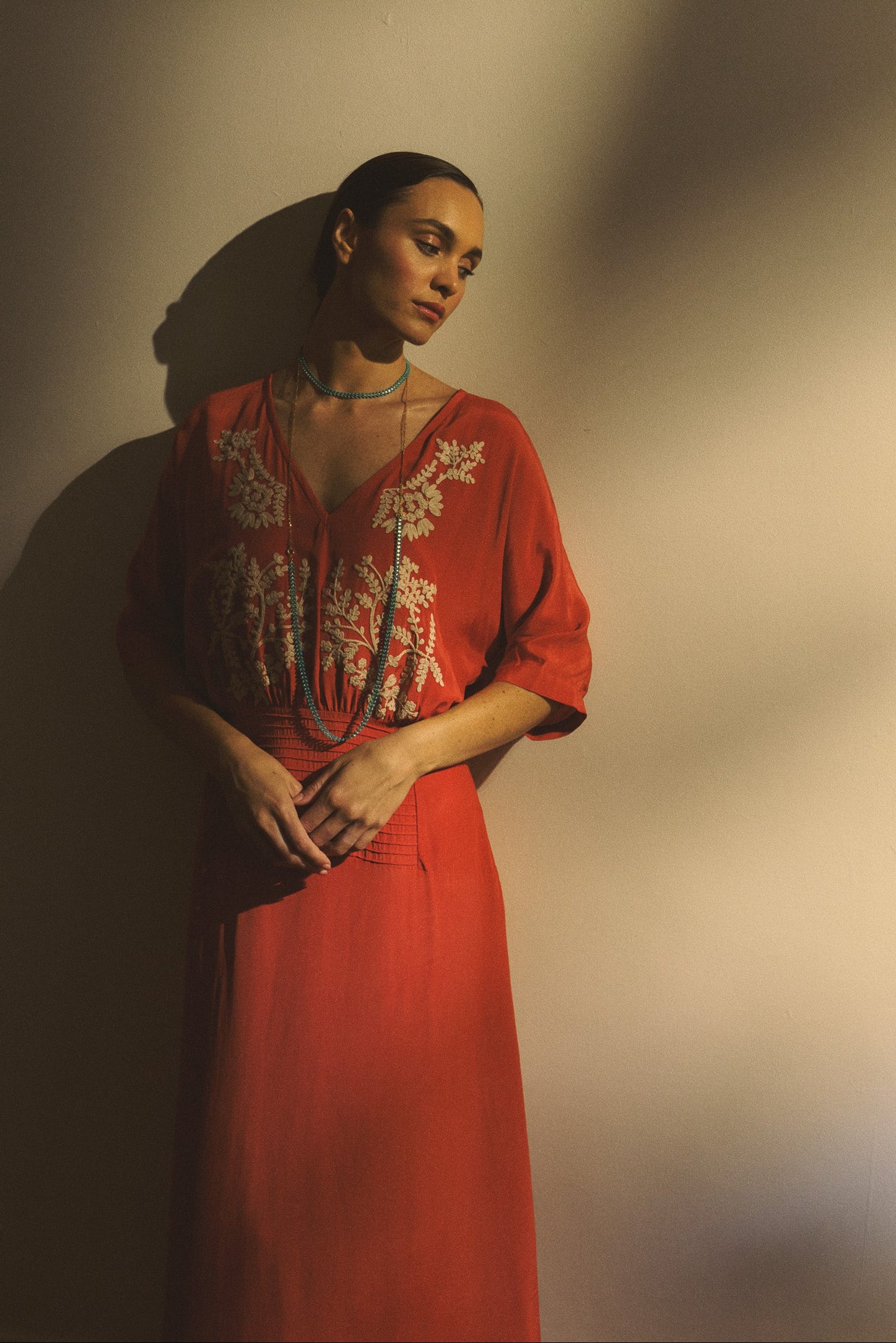 Woman wearing a red dress with floral embroidery against a plain background