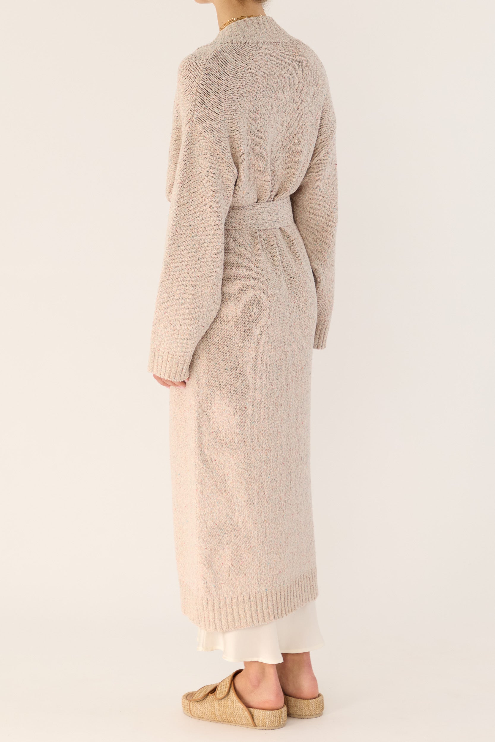 Model wearing beige knitted longline cardigan and white silk slip, back-side view