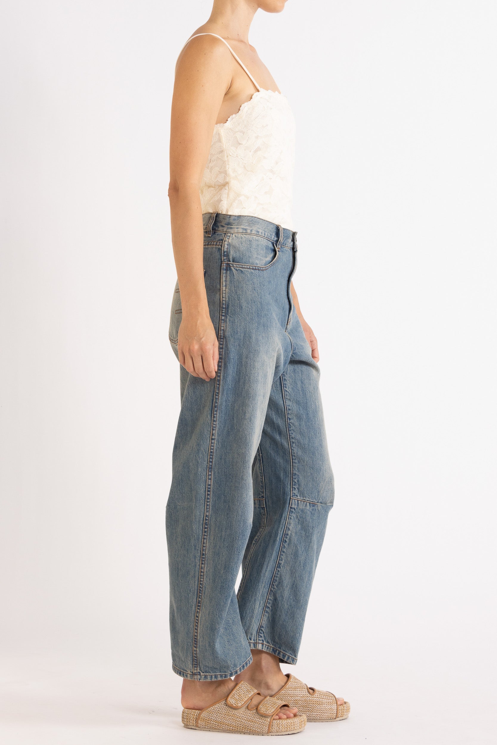 Woman wearing white floral lace camisole with blue denim bow-leg jeans with a white background