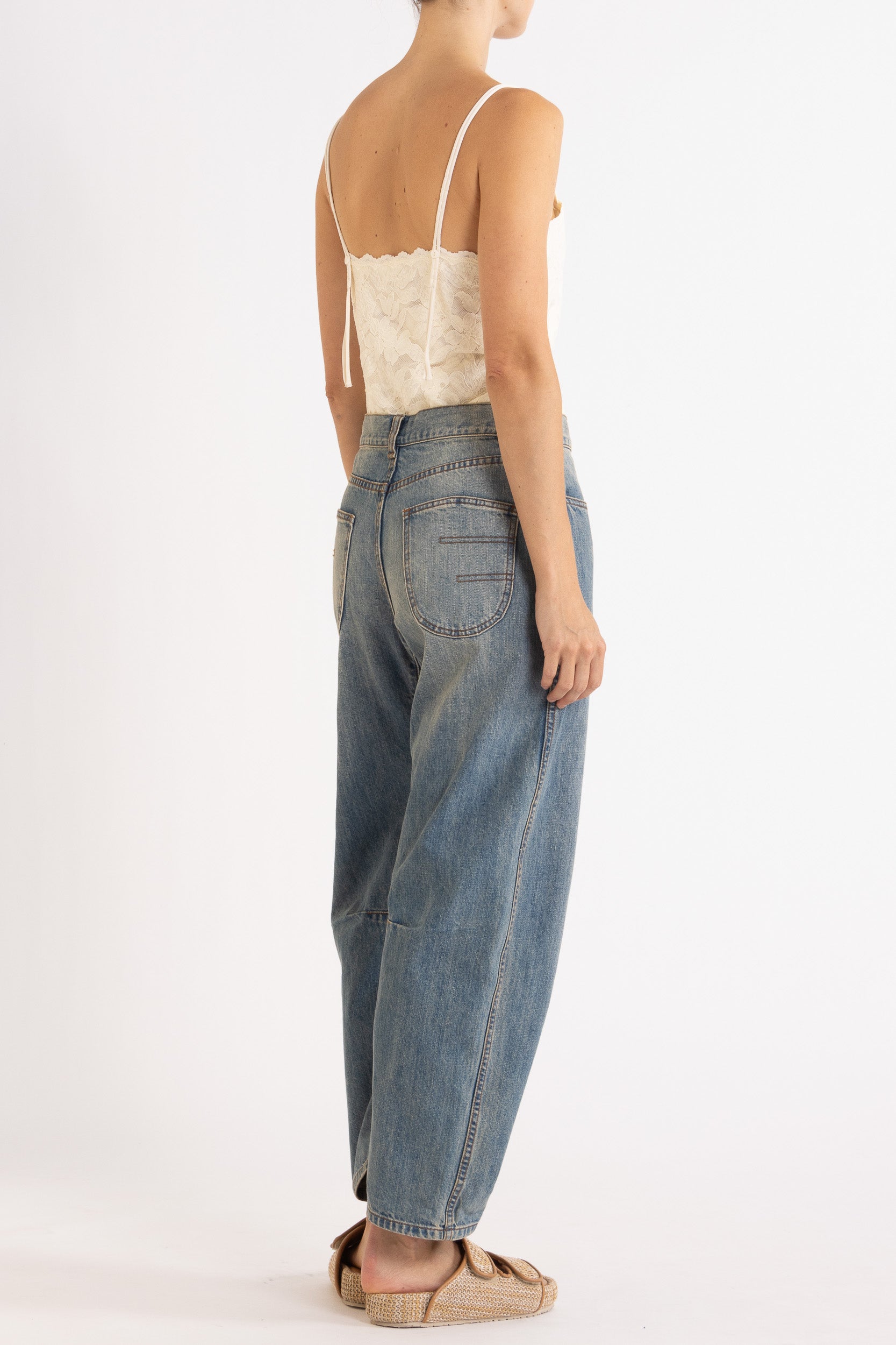 Woman wearing white floral lace camisole with blue denim bow-leg jeans with a white background