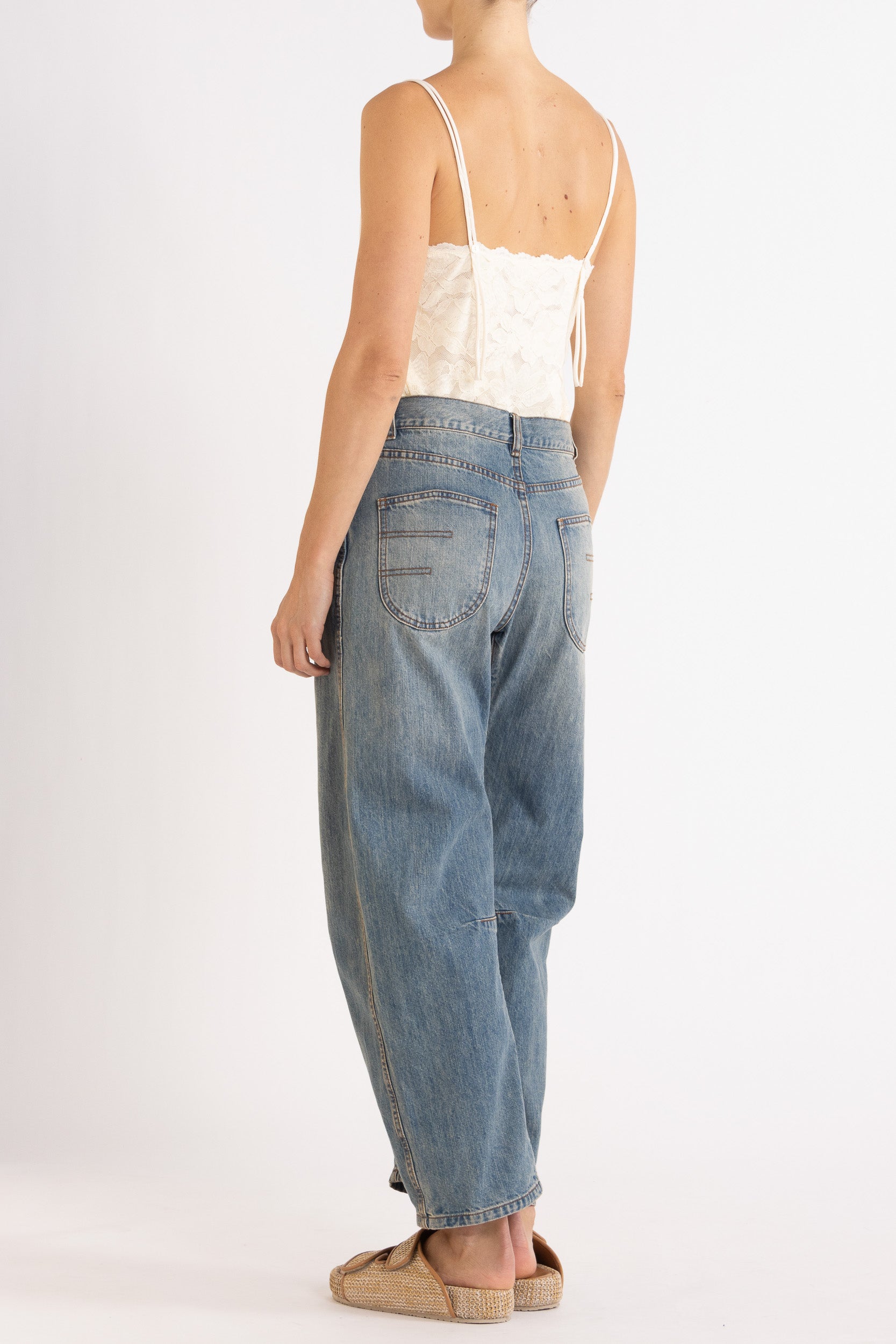 Woman wearing white floral lace camisole with blue denim bow-leg jeans with a white background