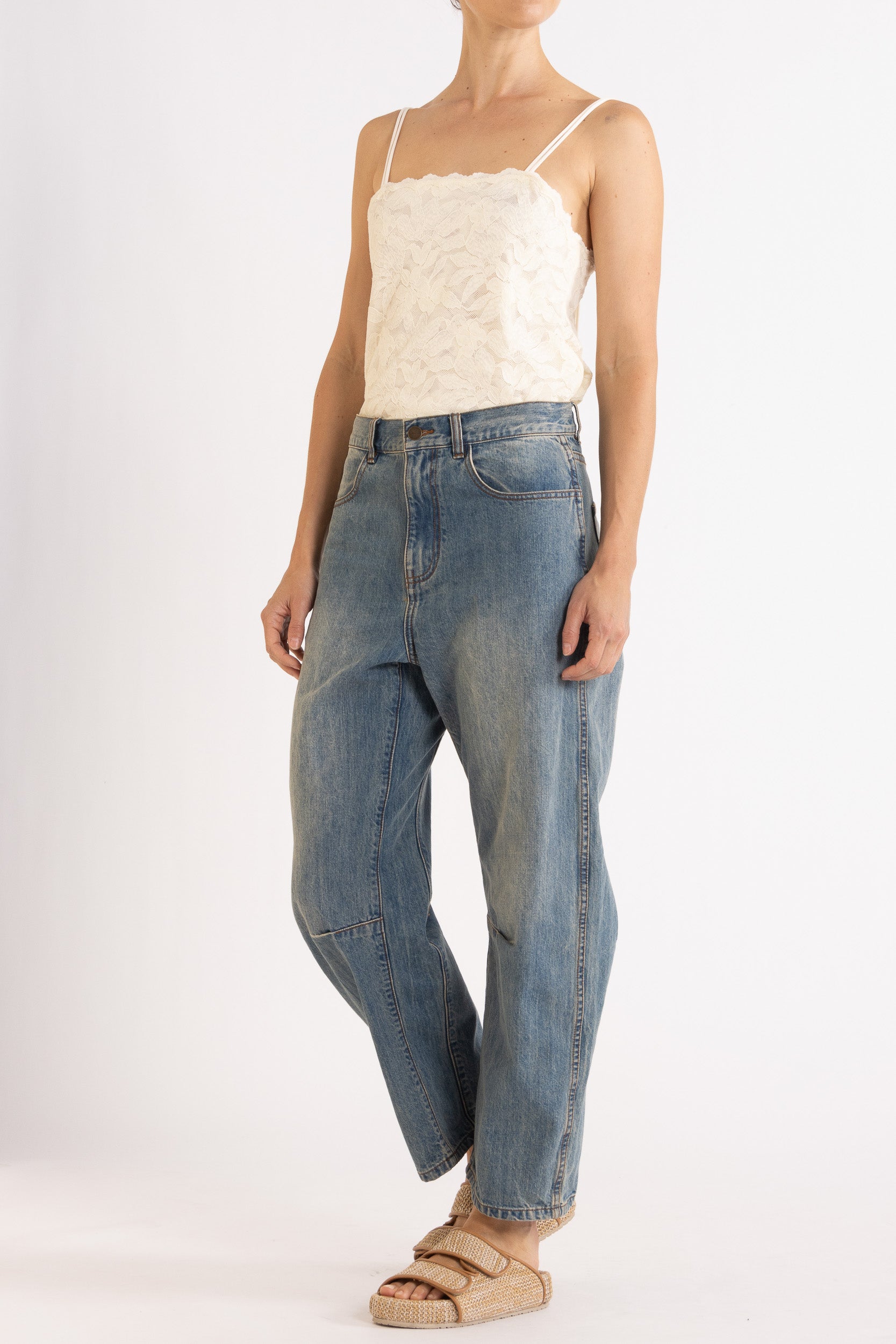 Woman wearing white floral lace camisole with blue denim bow-leg jeans with a white background