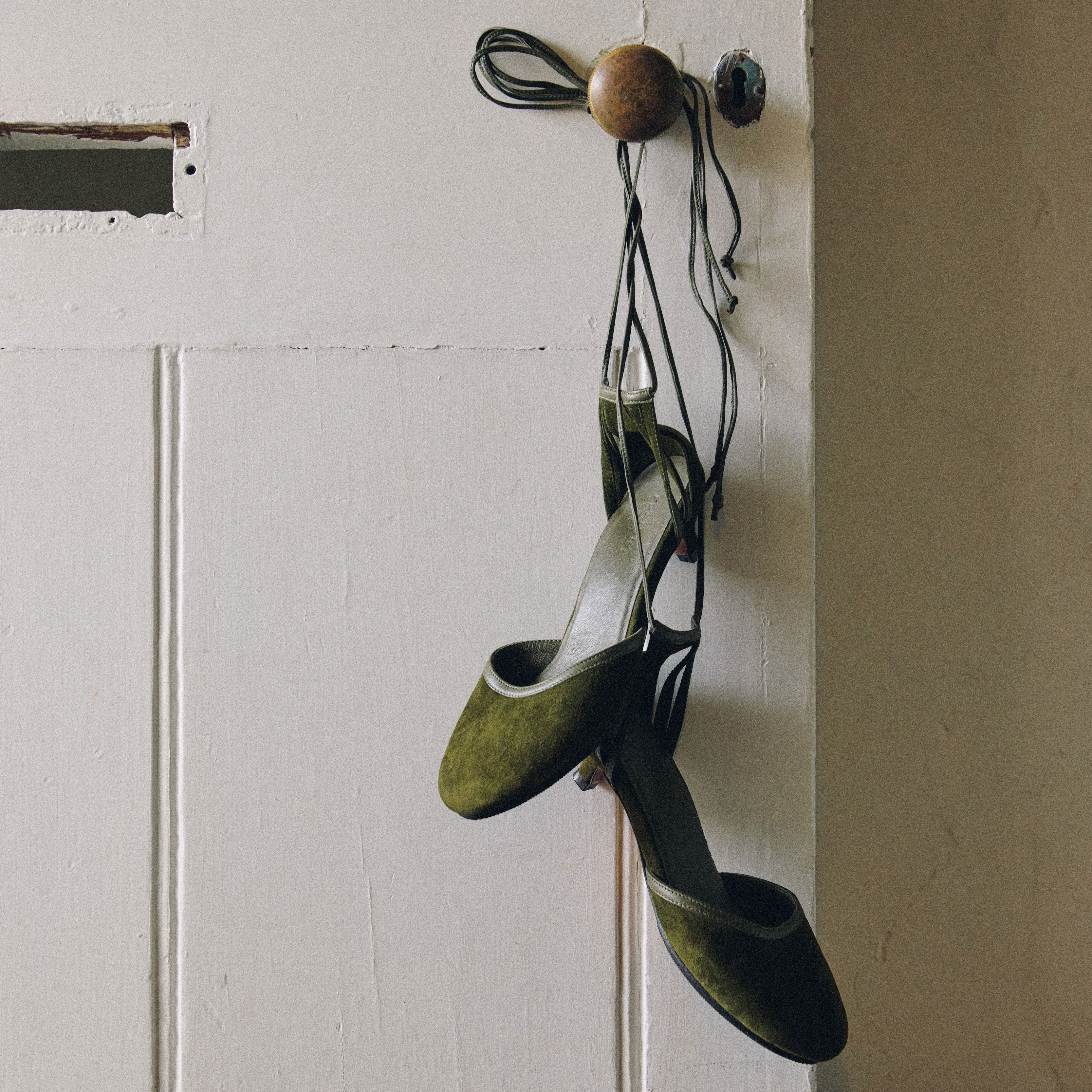 Green tango-heels hanging on a hook against a white wall.