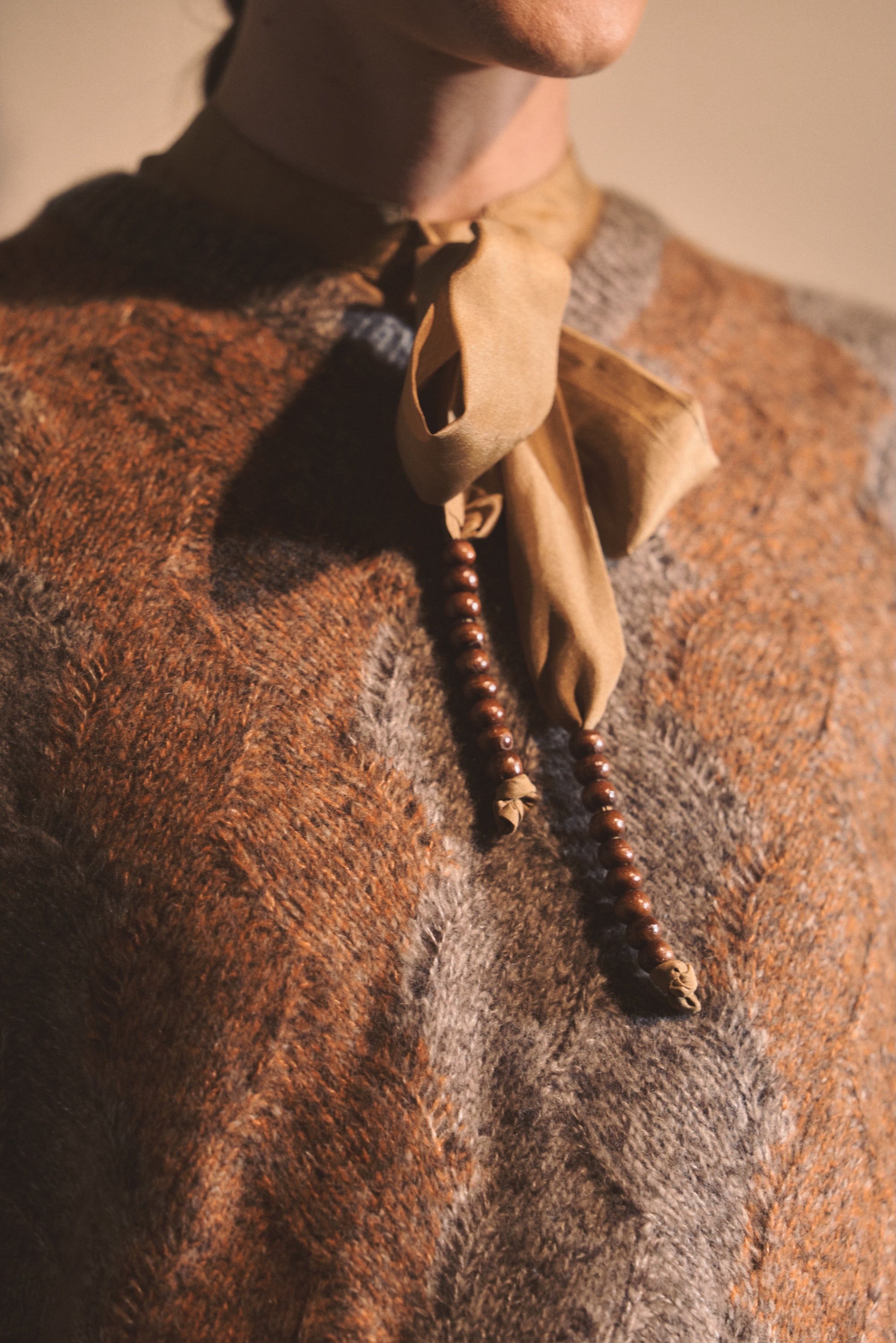 Close up image of model wearing a knitted vest and silk top with beaded tassel ties. 