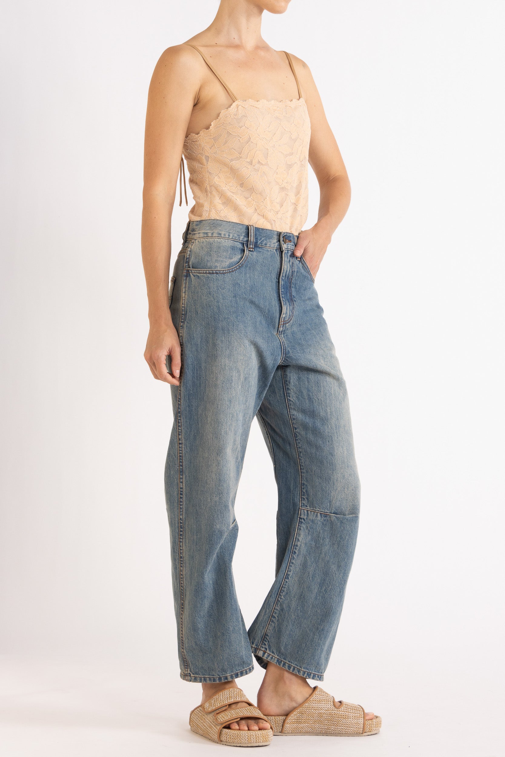 Woman wearing a floral lace camisole in biscuit colour way paired with denim bow-leg jeans with a white background