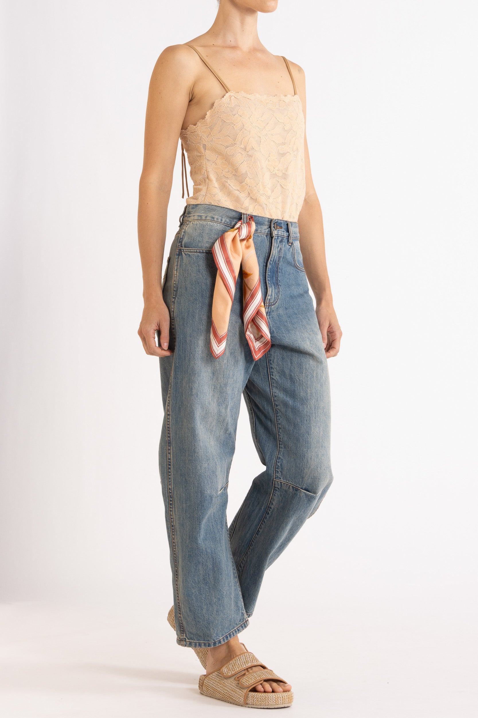 Woman wearing a floral lace camisole in biscuit colour way paired with denim bow-leg jeans and a honey print scarf with a white background