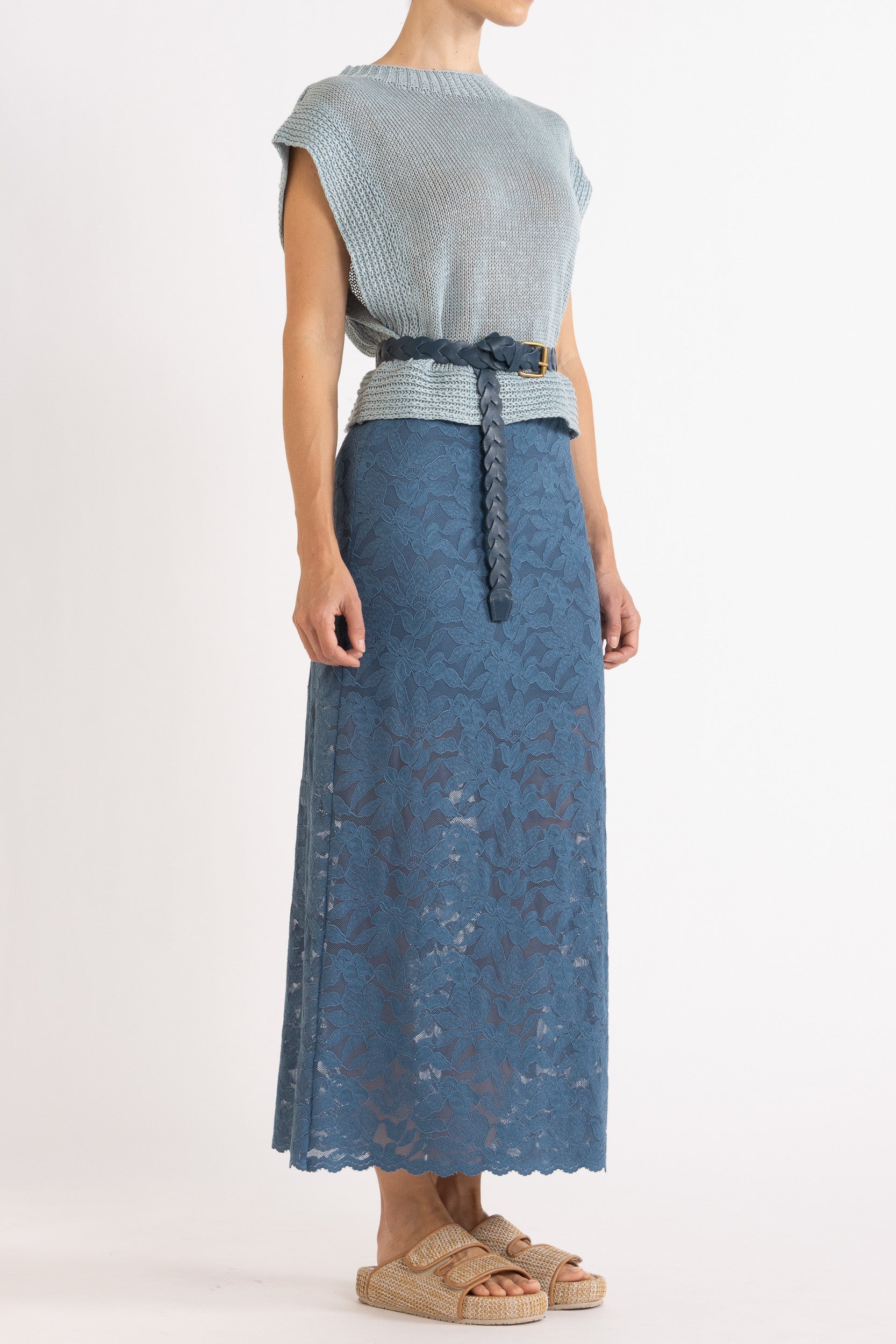 Woman wearing blue linen vest with a braided blue belt and a blue floral lace skirt.