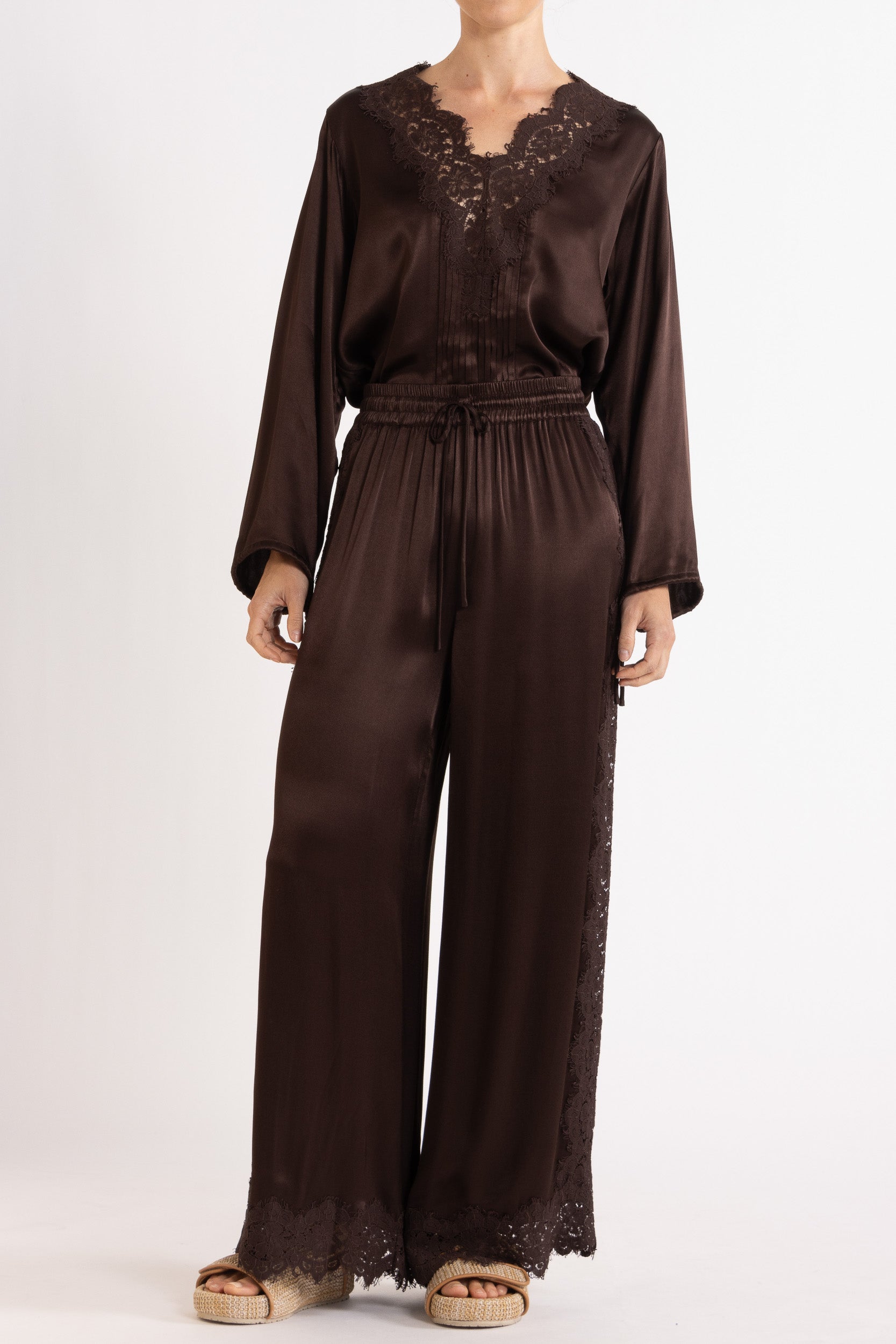Woman wearing a brown long sleeve top and pant with lace details on a white background