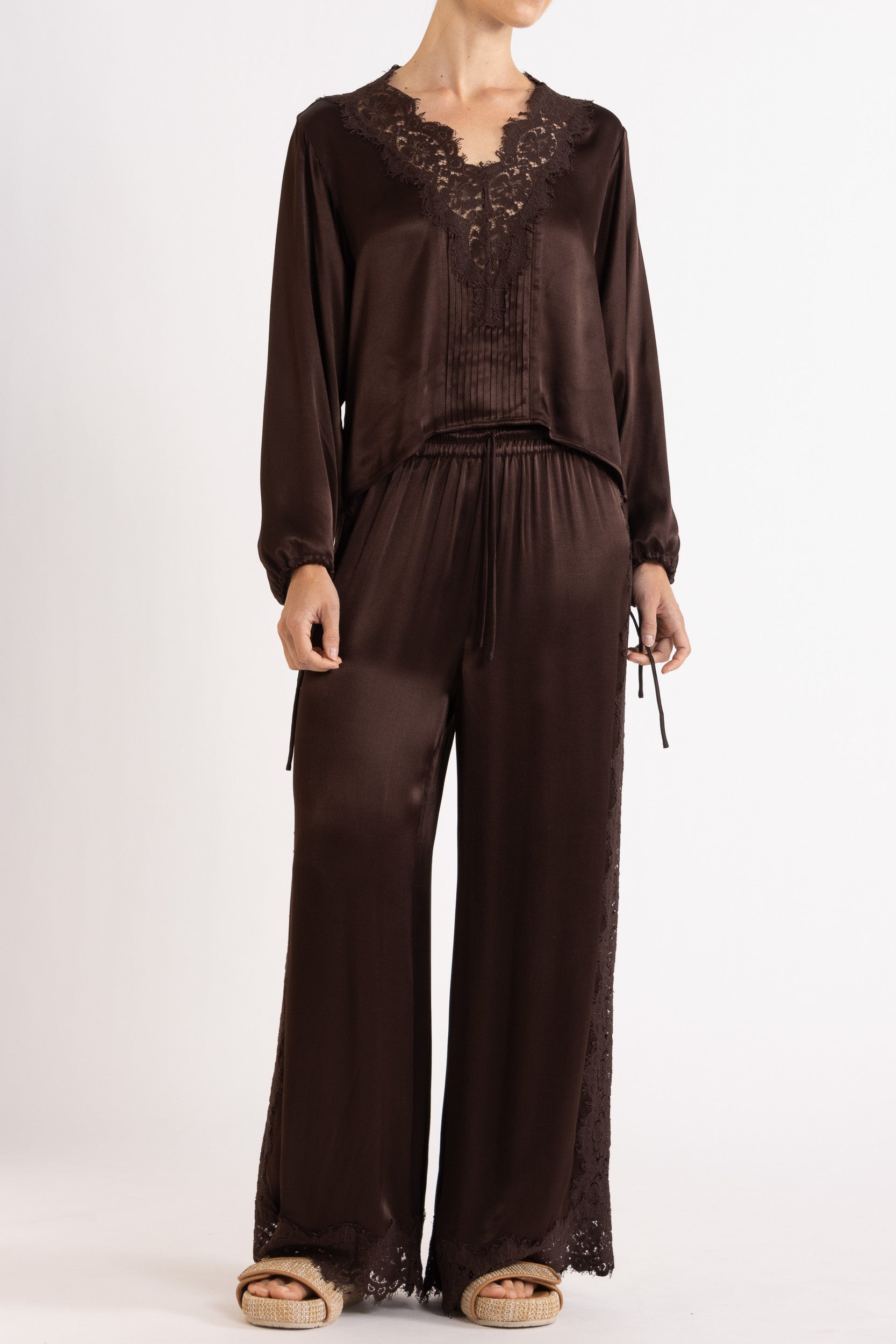 Woman wearing a brown long sleeve top and pant with lace details on a white background