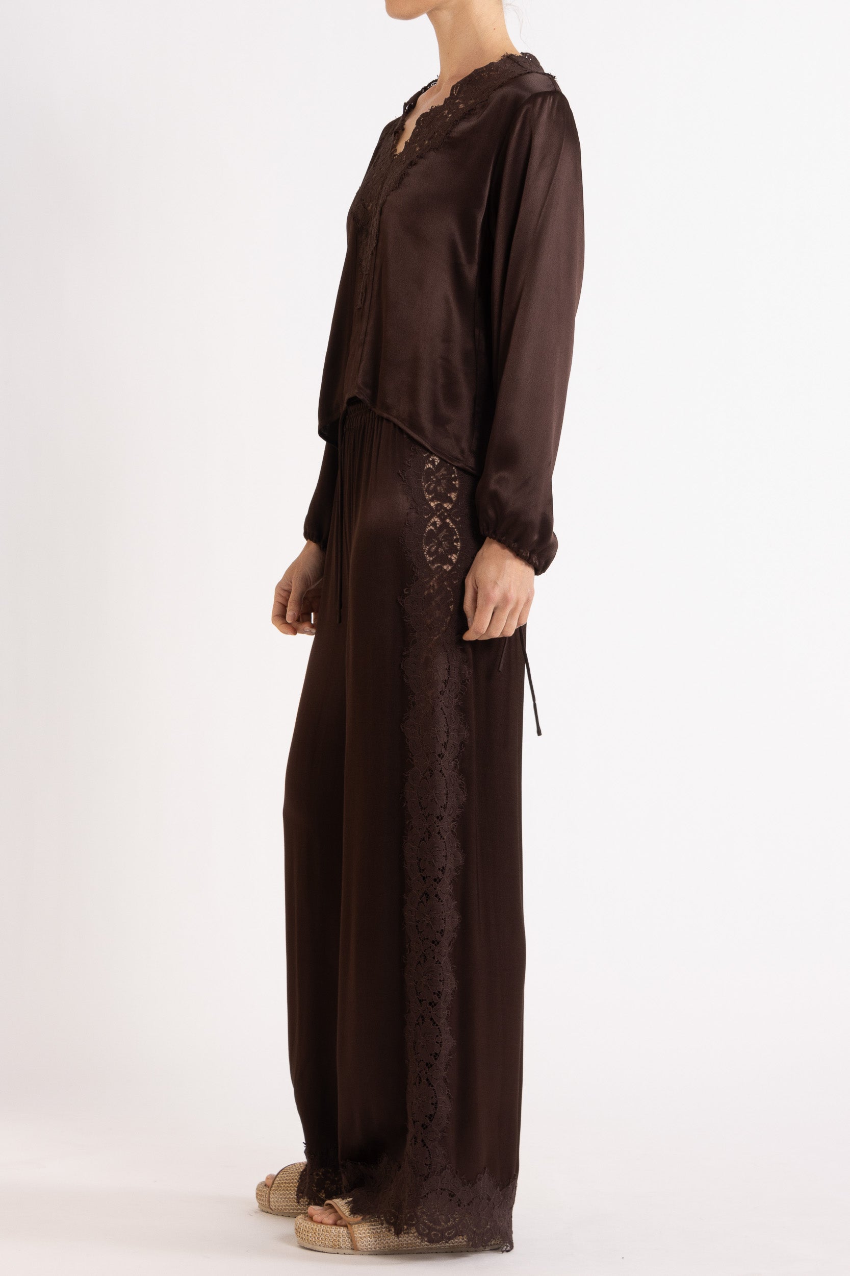 Woman wearing a brown long sleeve top and pant with lace details on a white background