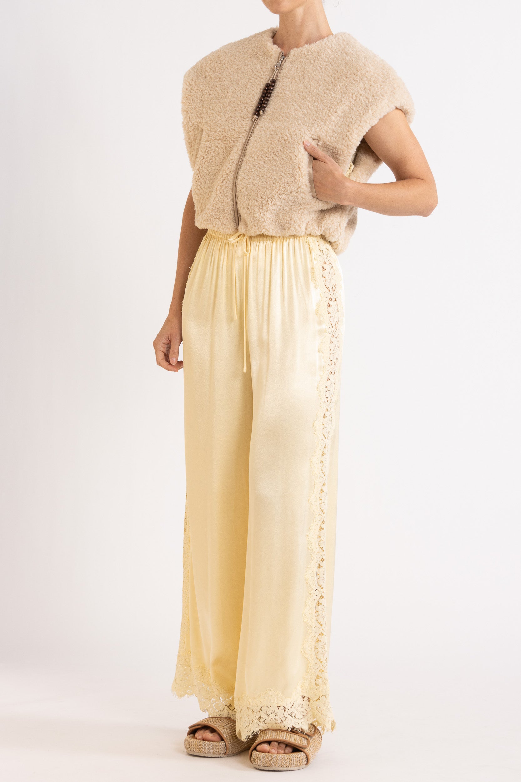 Woman wearing oat colour faux fur zip up vest with vanilla lace-trimmed pants