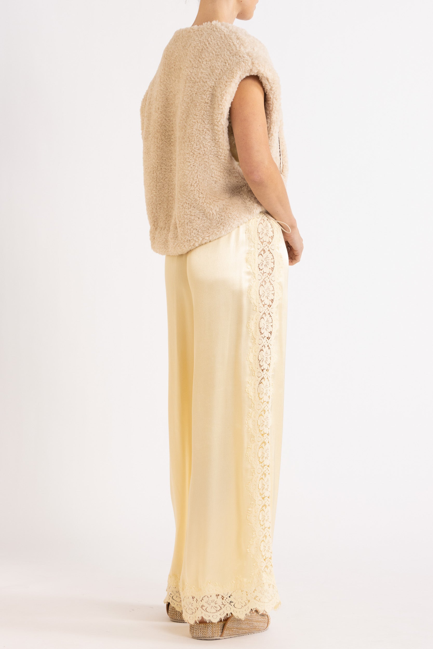Woman wearing oat colour faux fur zip up vest with vanilla lace-trimmed pants