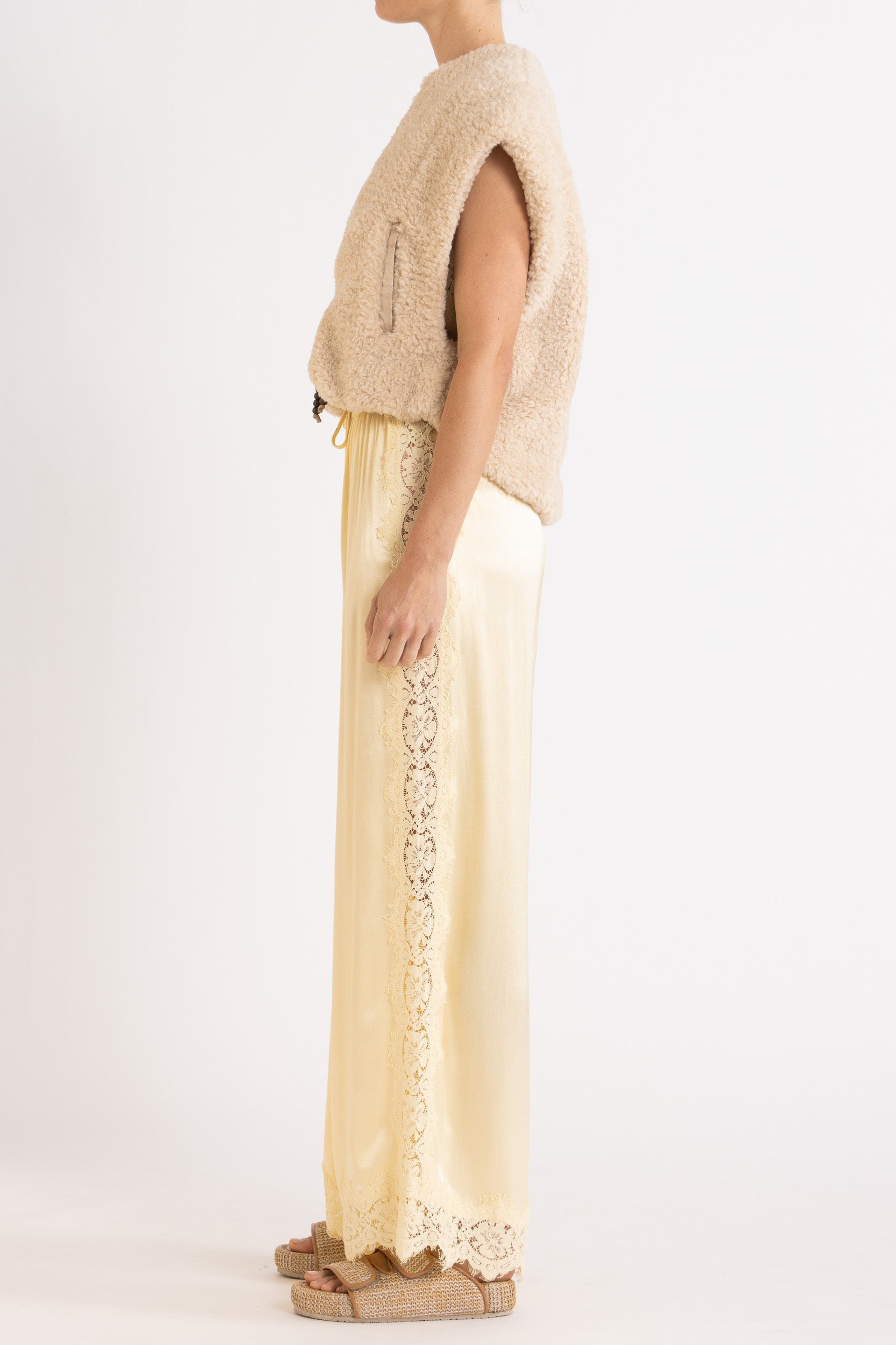 Woman wearing oat colour faux fur zip up vest with vanilla lace-trimmed pants