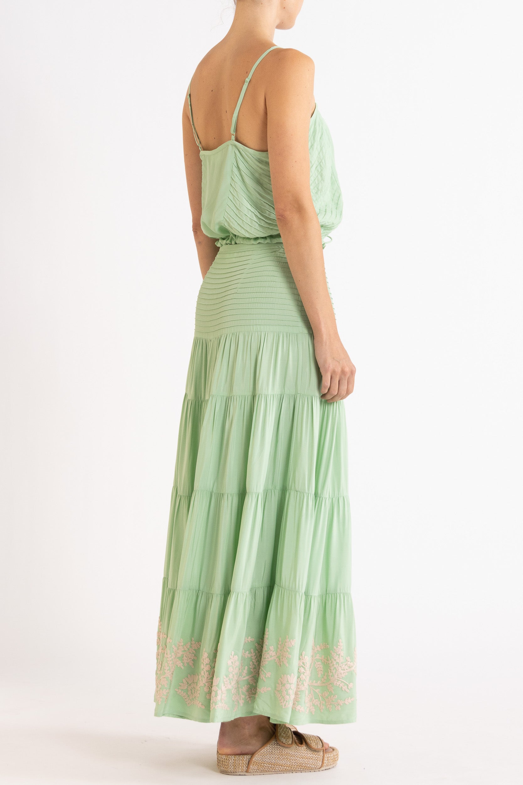 Woman wearing a mint green camisole and long, tiered skirt with white floral embroidery on a white background