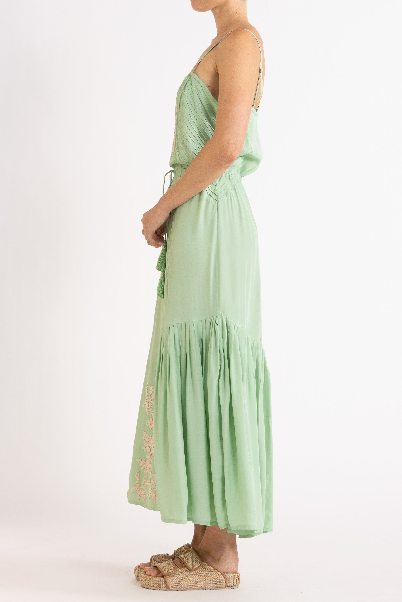 Woman wearing a light green dress with floral embroidery on a white background