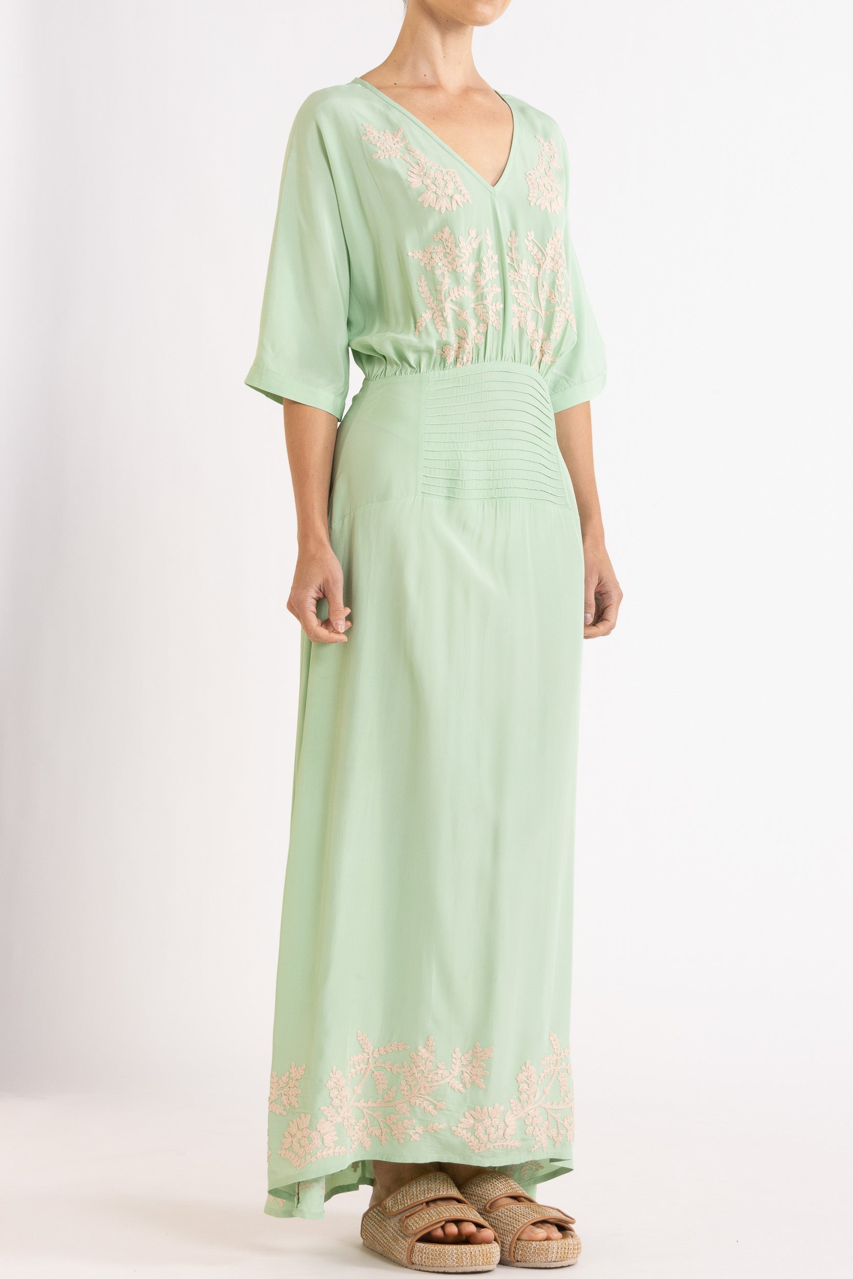 Woman wearing a light green dress with floral embroidery on a white background