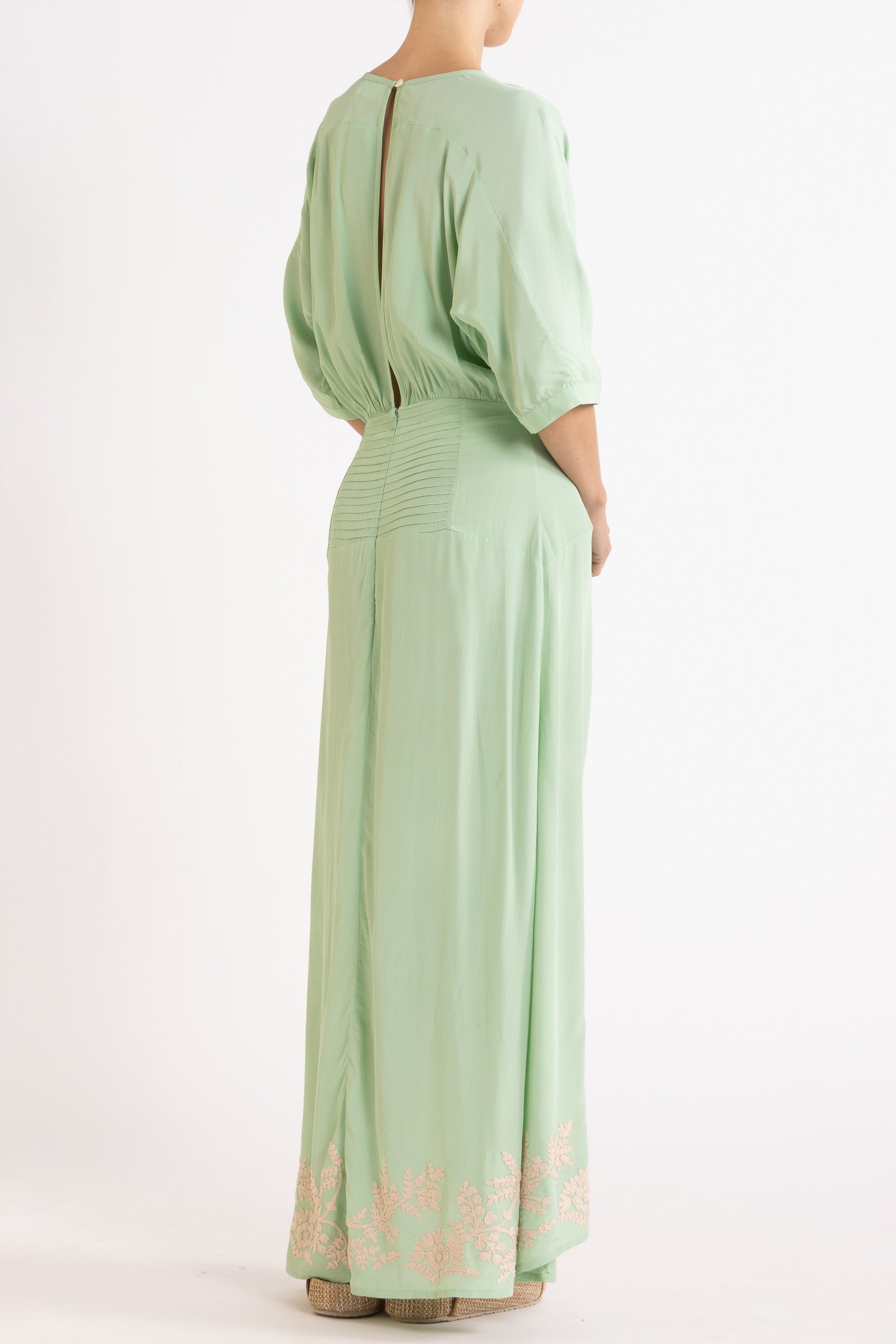 Woman wearing a light green dress with floral embroidery on a white background