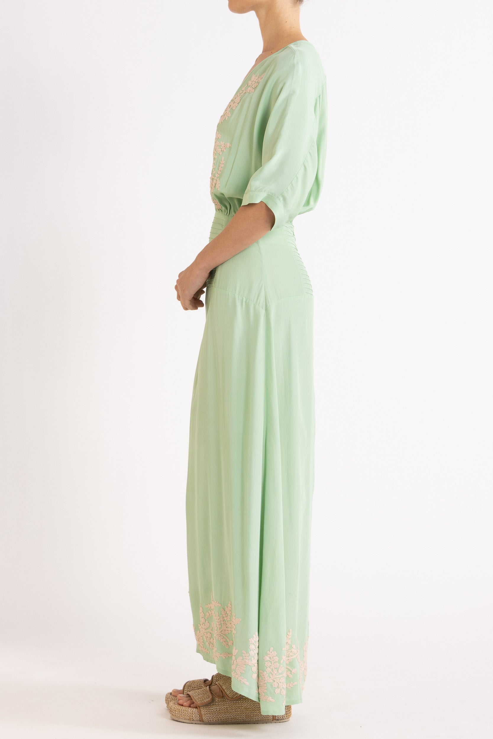 Woman wearing a light green dress with floral embroidery on a white background