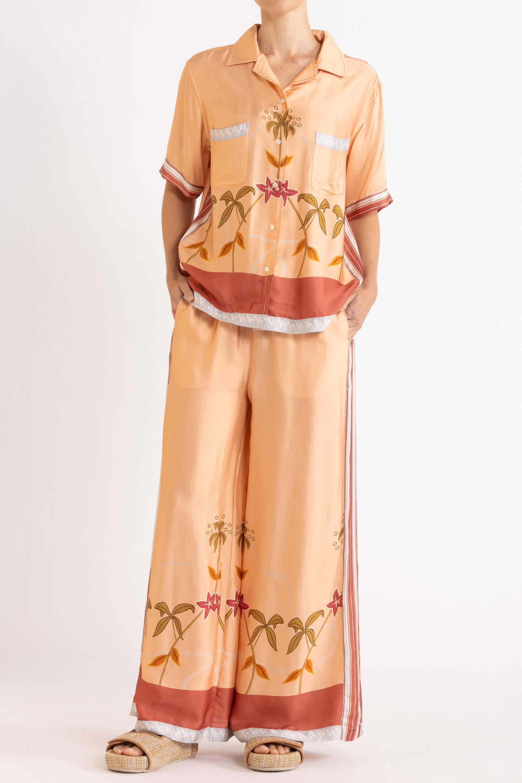 Woman wearing a matching peach short sleeve shirt and pants featuring floral patterns on a white background
