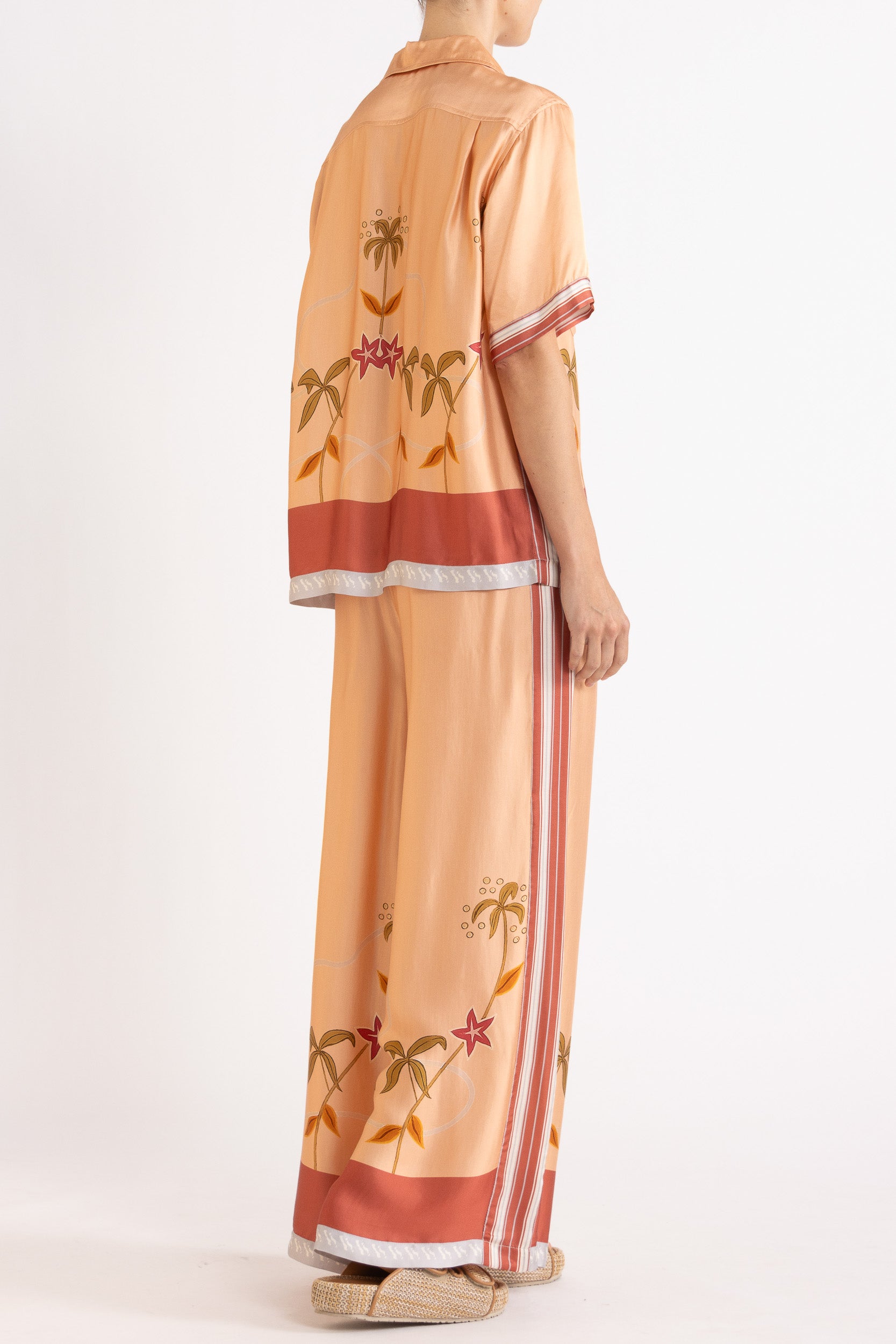 Woman wearing a matching peach short sleeve shirt and pants featuring floral patterns on a white background
