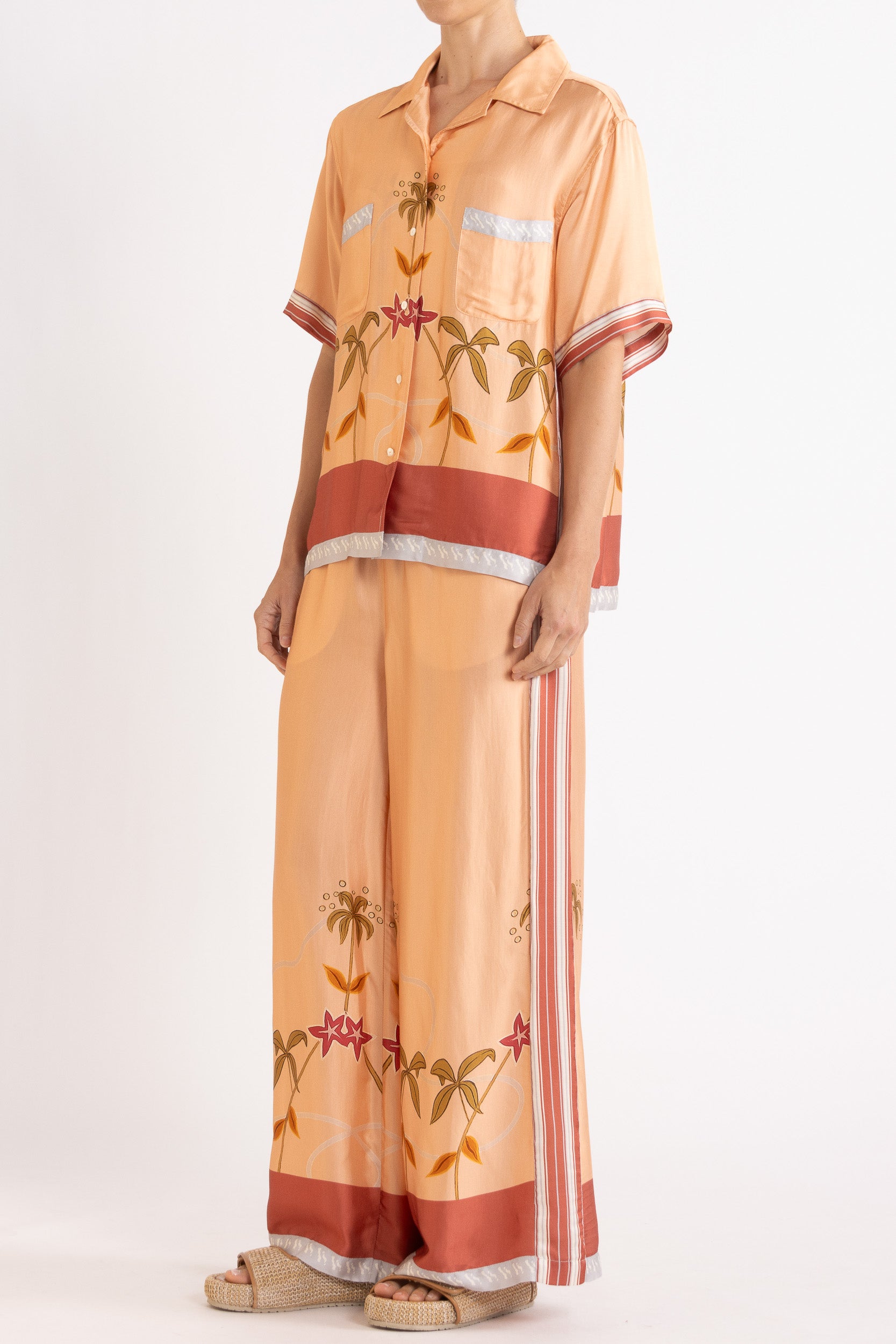 Woman wearing a matching peach short sleeve shirt and pants featuring floral patterns on a white background