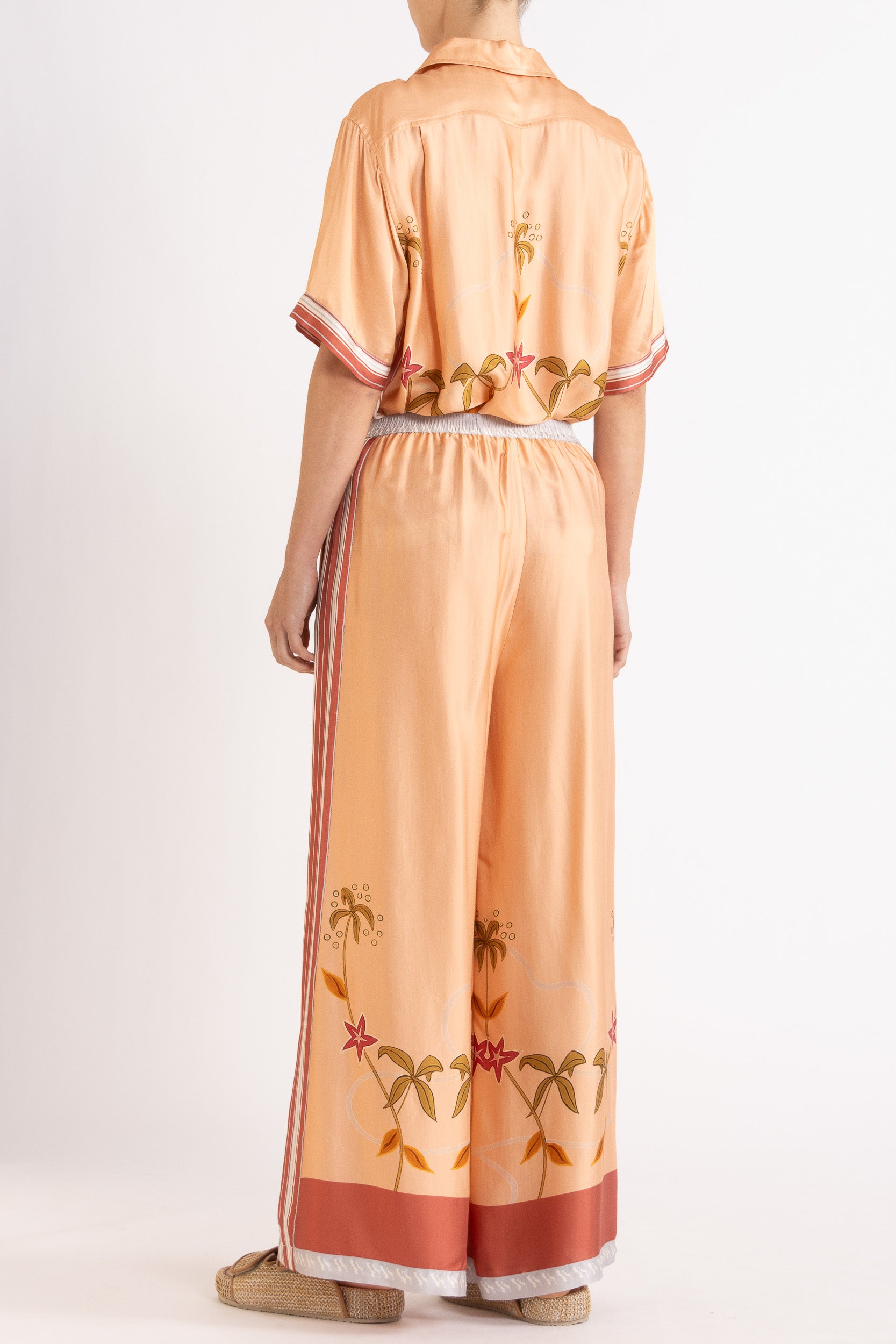 Woman wearing a matching peach short sleeve shirt and pants featuring floral patterns on a white background