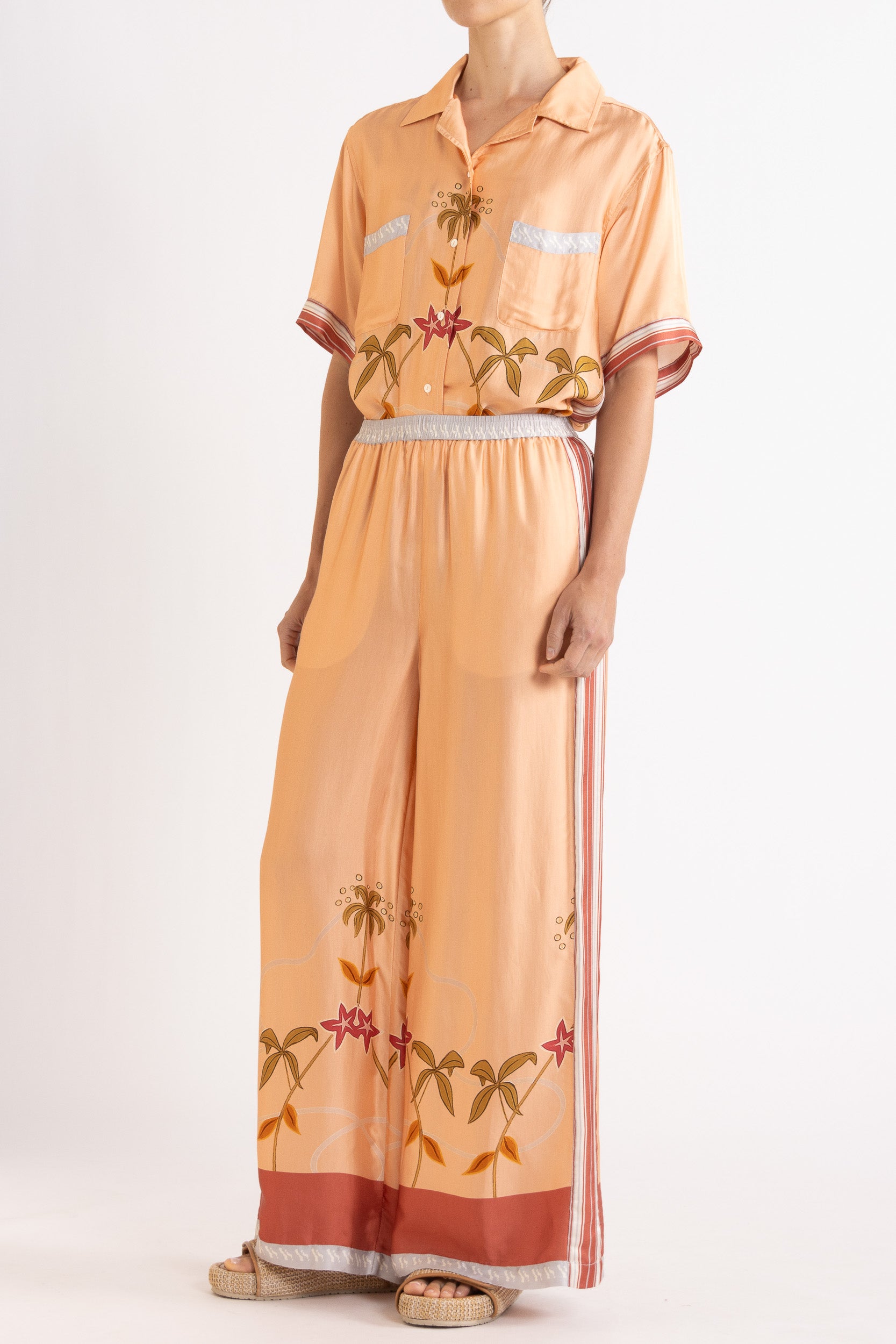 Woman wearing a matching peach short sleeve shirt and pants featuring floral patterns on a white background