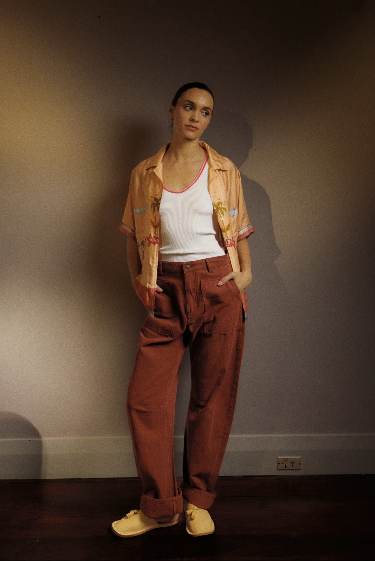 Woman wearing a peach short sleeve shirt with floral patterns and red pants in an empty room