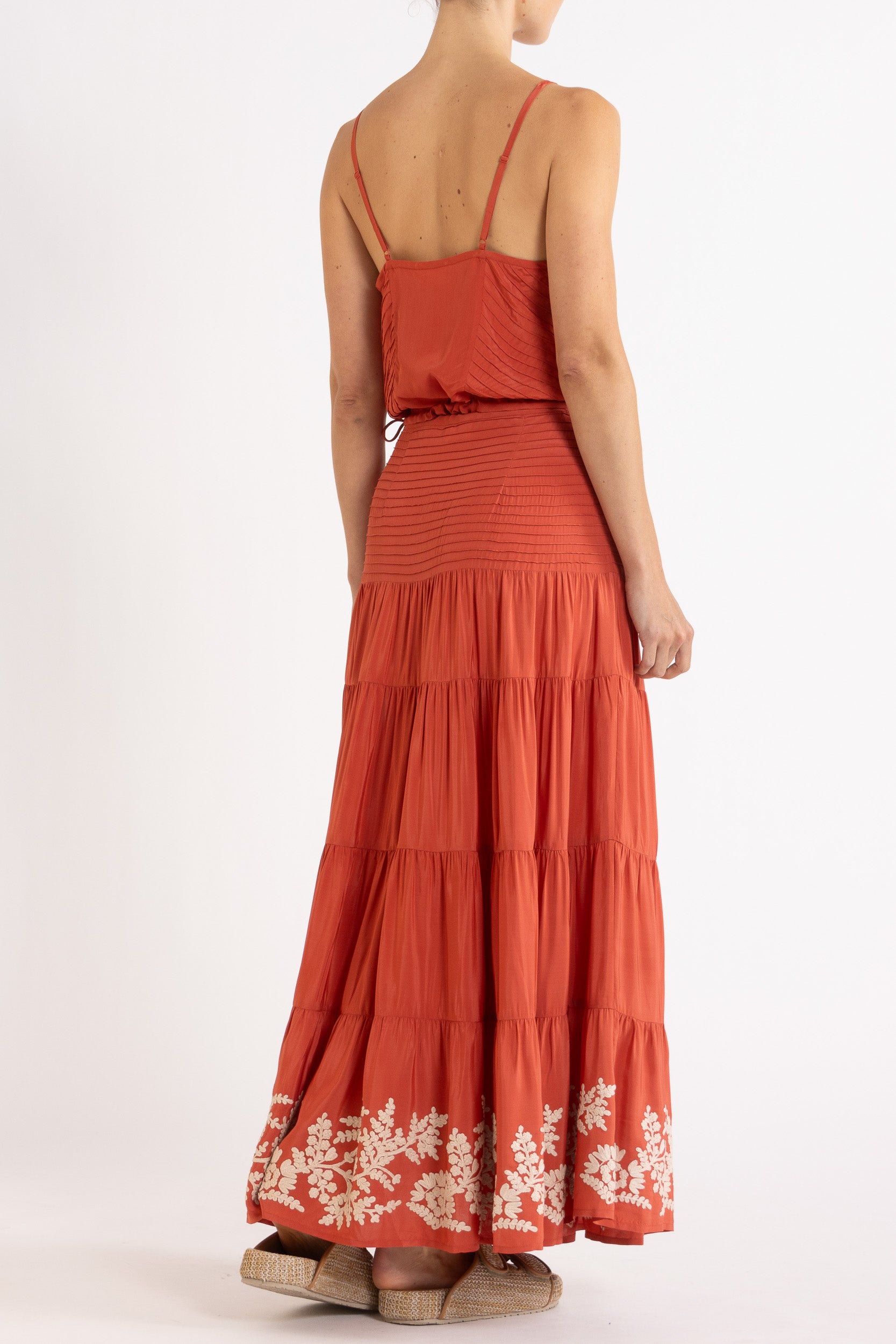 Woman wearing a red camisole and long, tiered skirt with white floral embroidery on a white background
