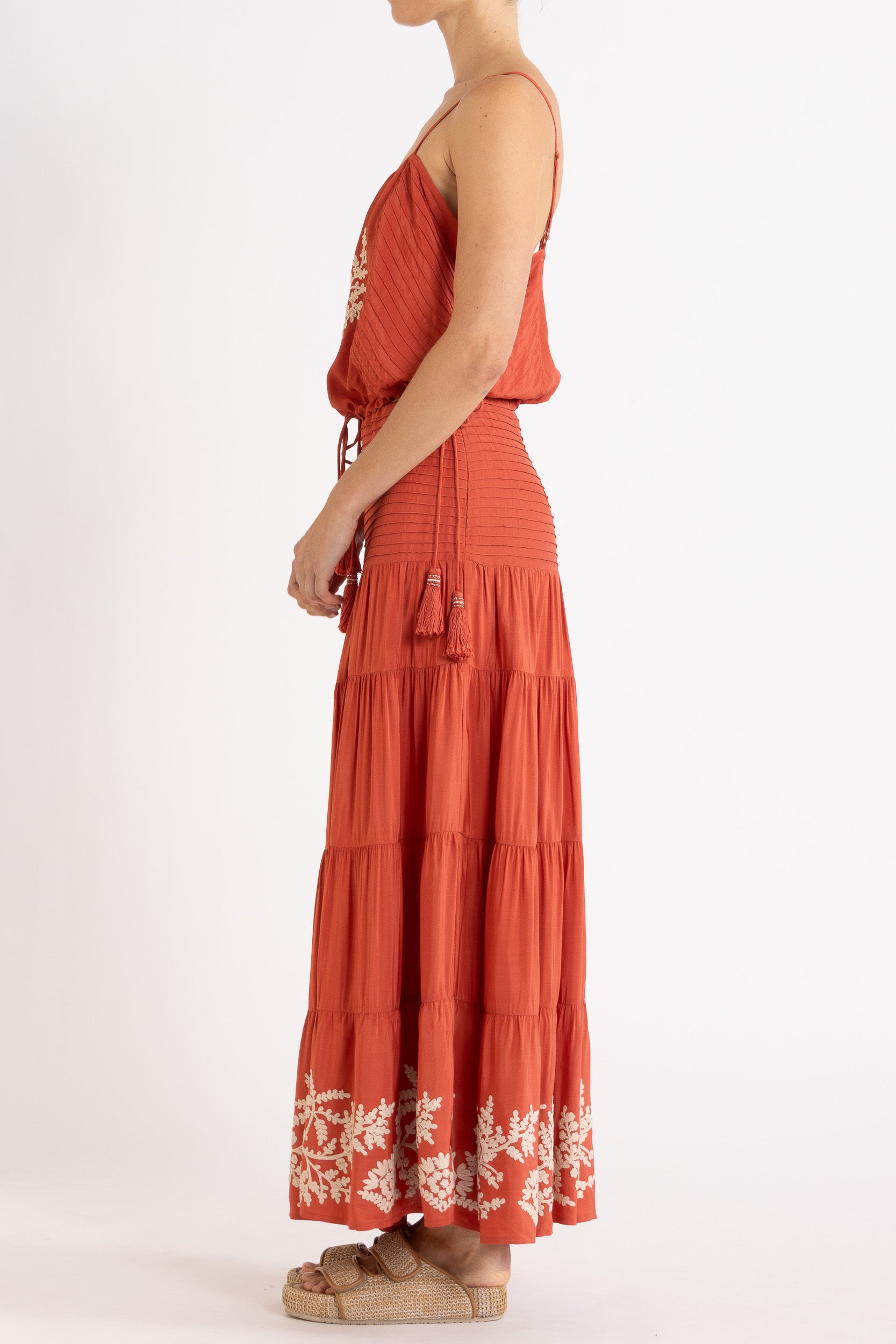 Woman wearing a red camisole and long, tiered skirt with white floral embroidery on a white background