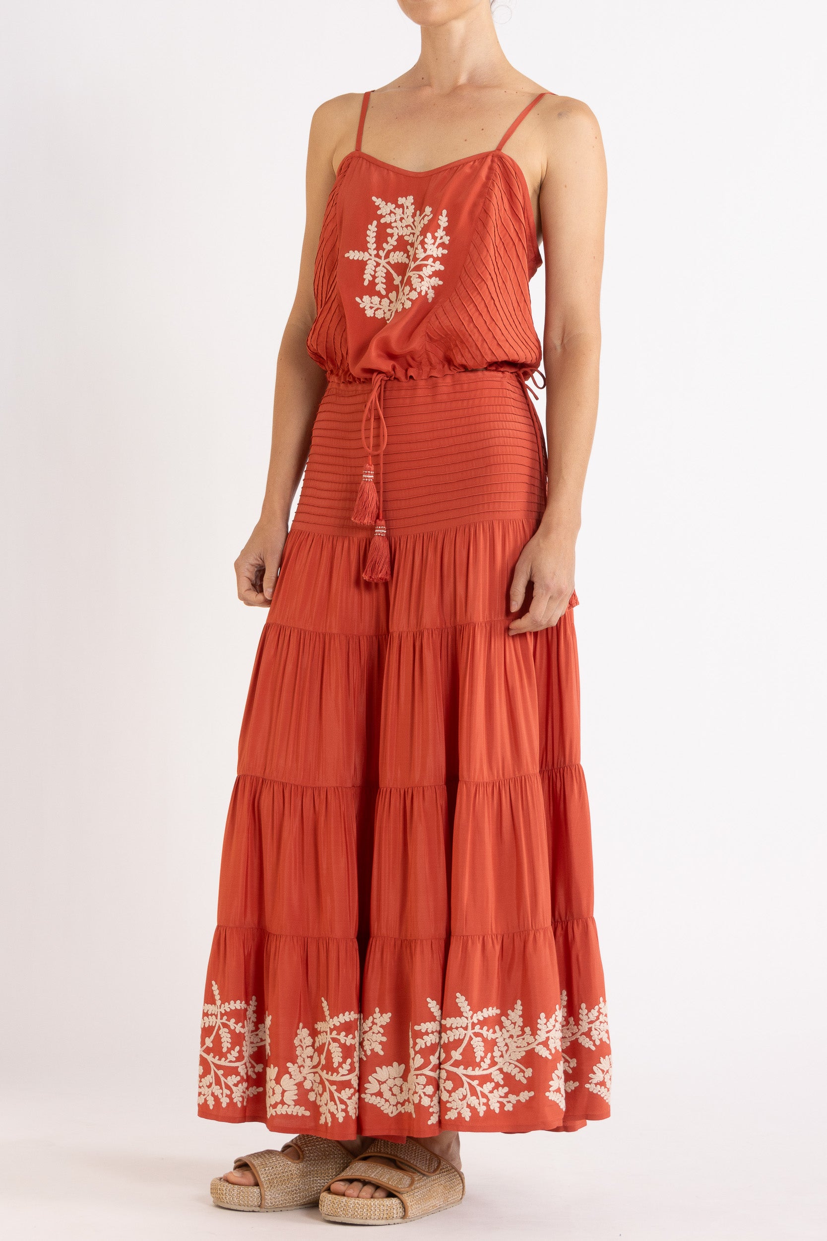 Woman wearing a red camisole and long, tiered skirt with white floral embroidery on a white background