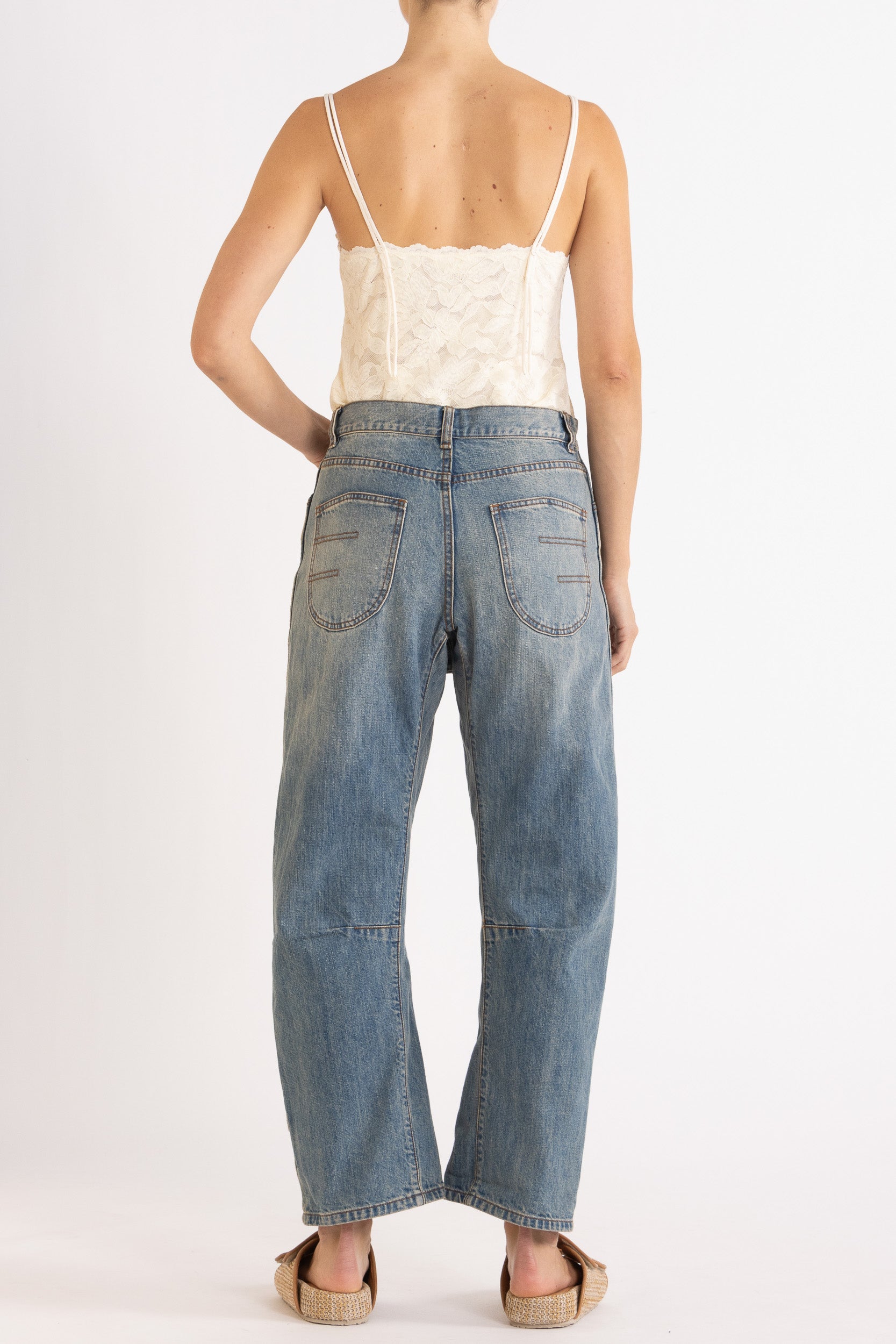 Woman wearing white floral lace camisole with blue denim bow-leg jeans with a white background